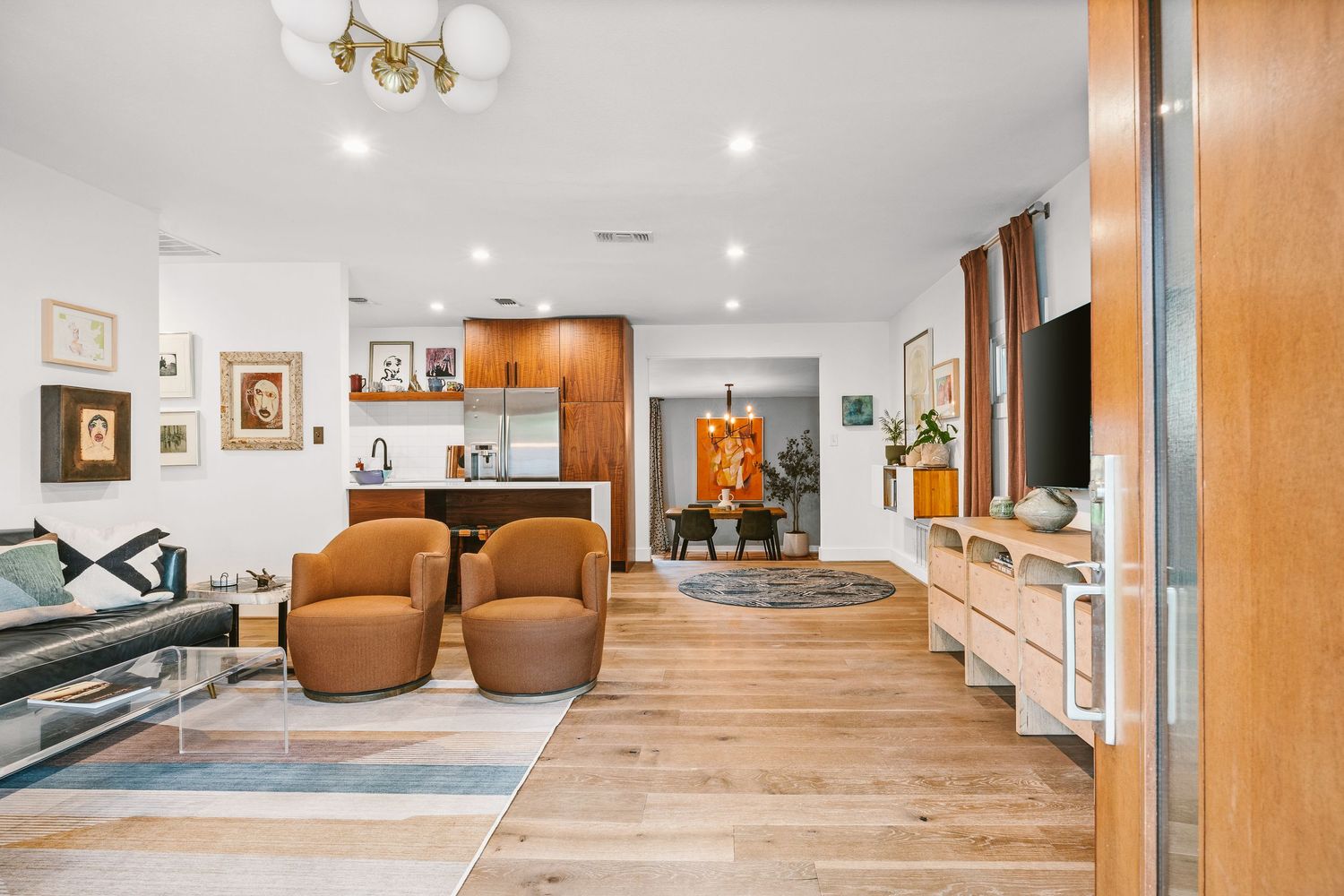 Modern open-plan living room with hardwood floors, brown leather chairs, wood cabinetry, and a flat-screen TV on a media console.