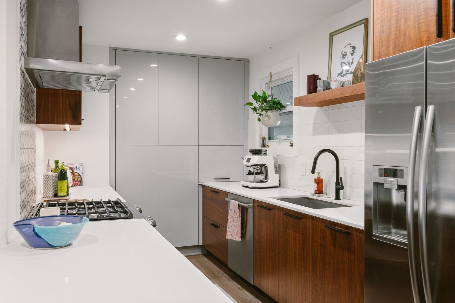 Modern kitchen with gray cabinets, walnut wood accents, stainless steel appliances, white countertops, and open shelving.