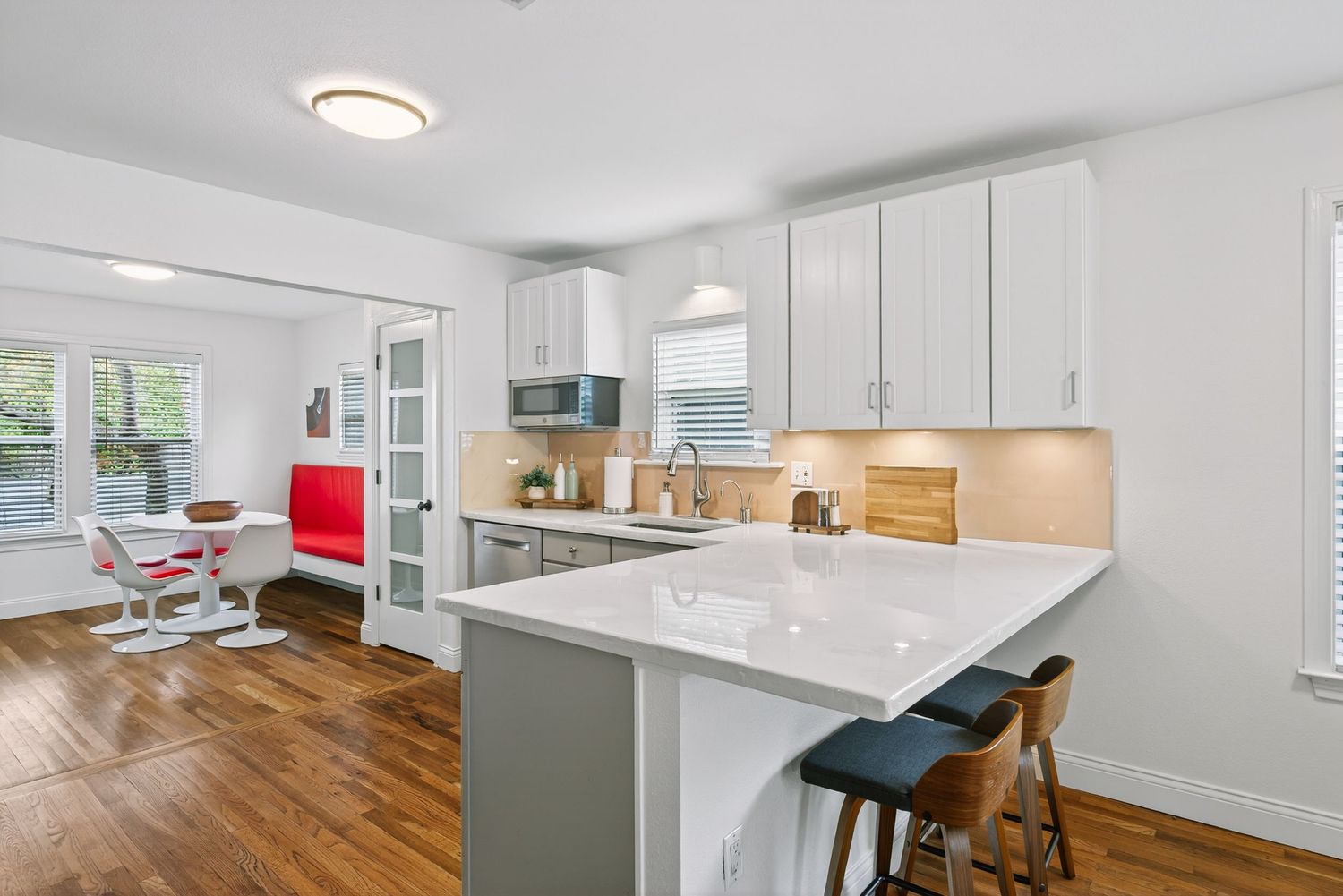 Modern white kitchen with marble peninsula, hardwood floors, and pendant lighting showcases sleek cabinetry and dining area.