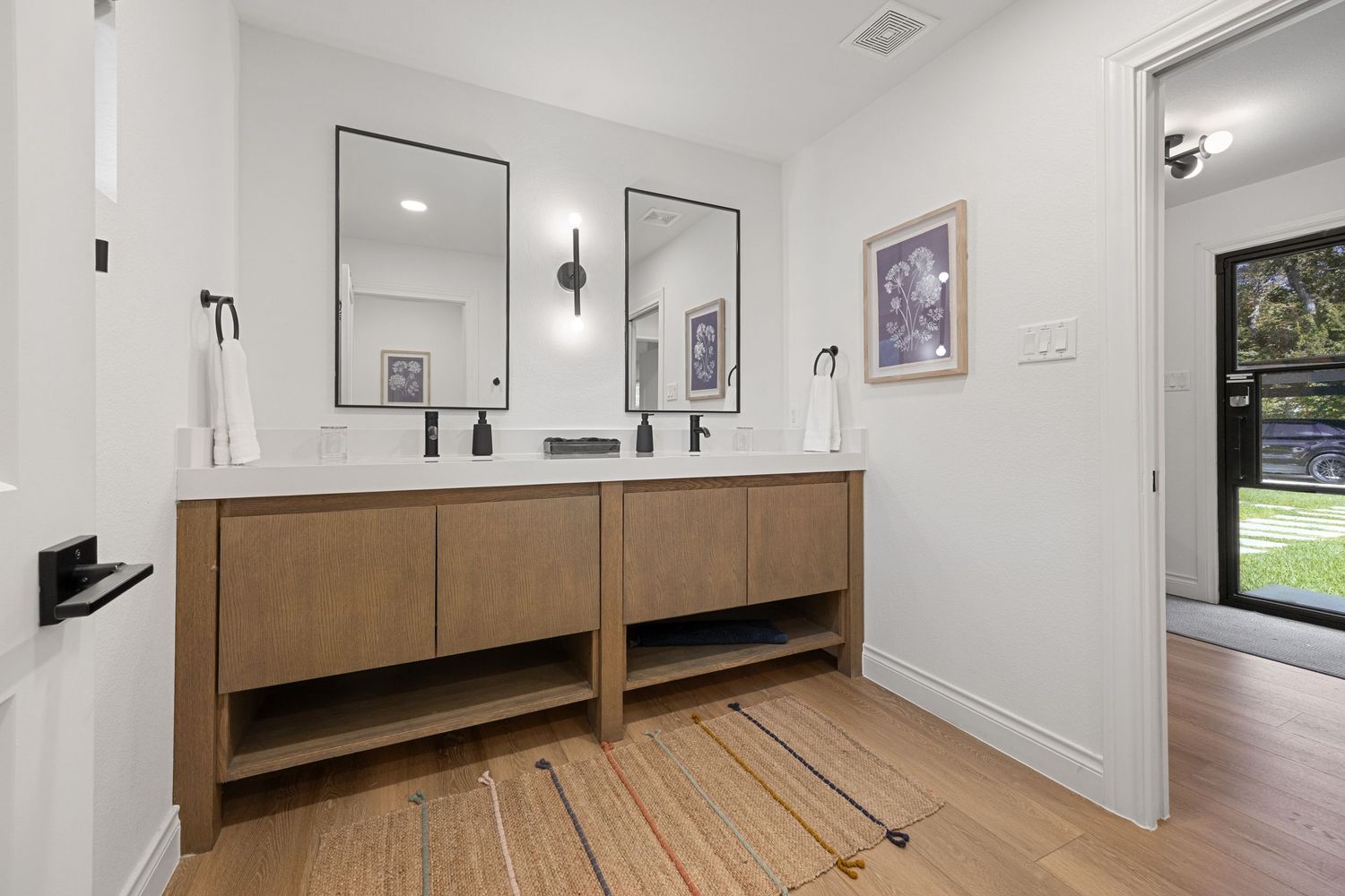 Bright double vanity bathroom with wood cabinets, dual black framed mirrors, white countertops, and hardwood floors.