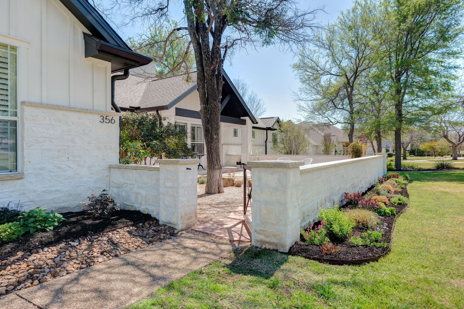 White brick home exterior with brick wall, manicured landscaping, mature trees, and brick pathway on a sunny day.