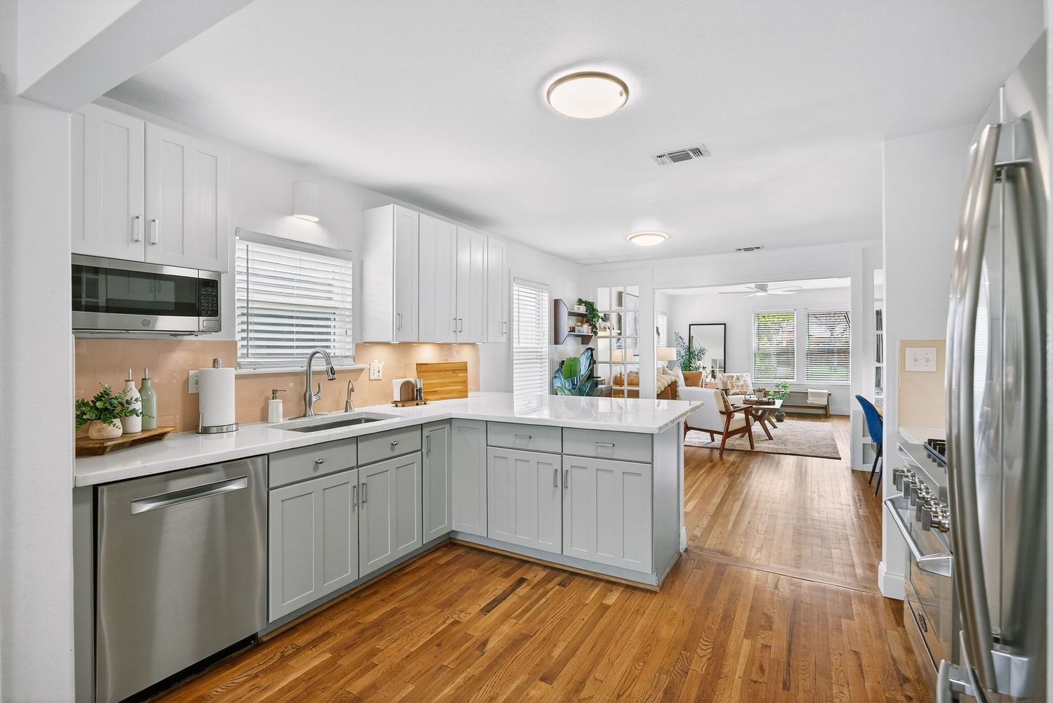 Modern kitchen with gray lower cabinets, white upper cabinets, and hardwood floors opening to living space.