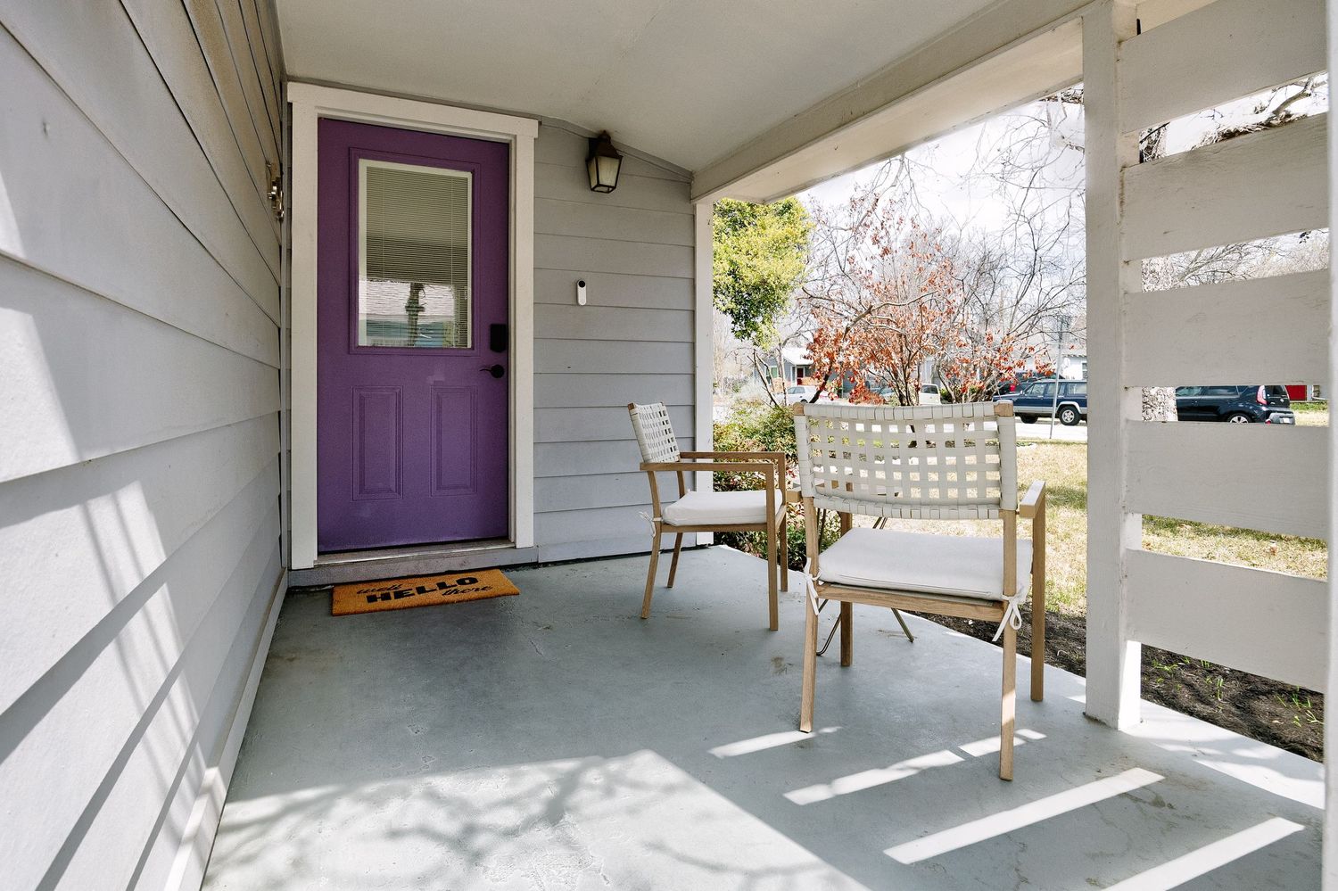 Bright sunlit interior hallway with white walls, hardwood floors, and purple accent door at the end.