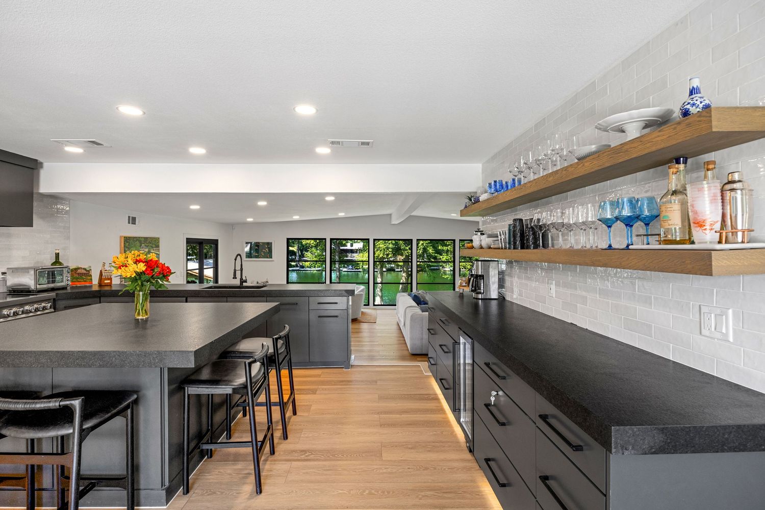 Modern kitchen featuring dark cabinetry, large island with seating, open shelving, and subway tile backsplash.