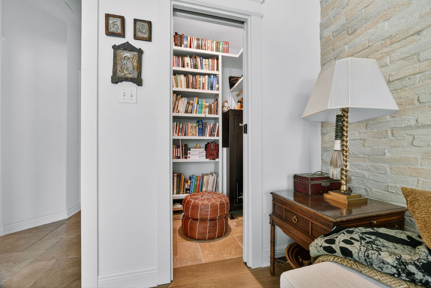 A cozy hallway leads to a built-in bookshelf library nook with colorful books, beside a wooden desk with a lamp.