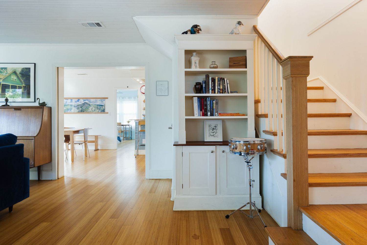 Modern open concept living space with white walls, hardwood floors and built-in shelving near a staircase.