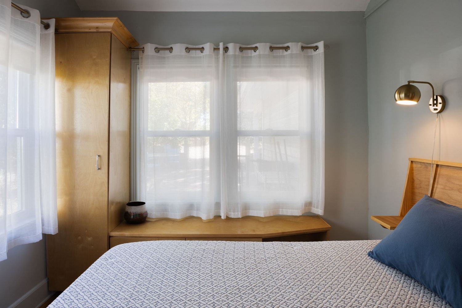 Modern bedroom featuring white curtains, gold wall sconce, and navy blue accent pillows.