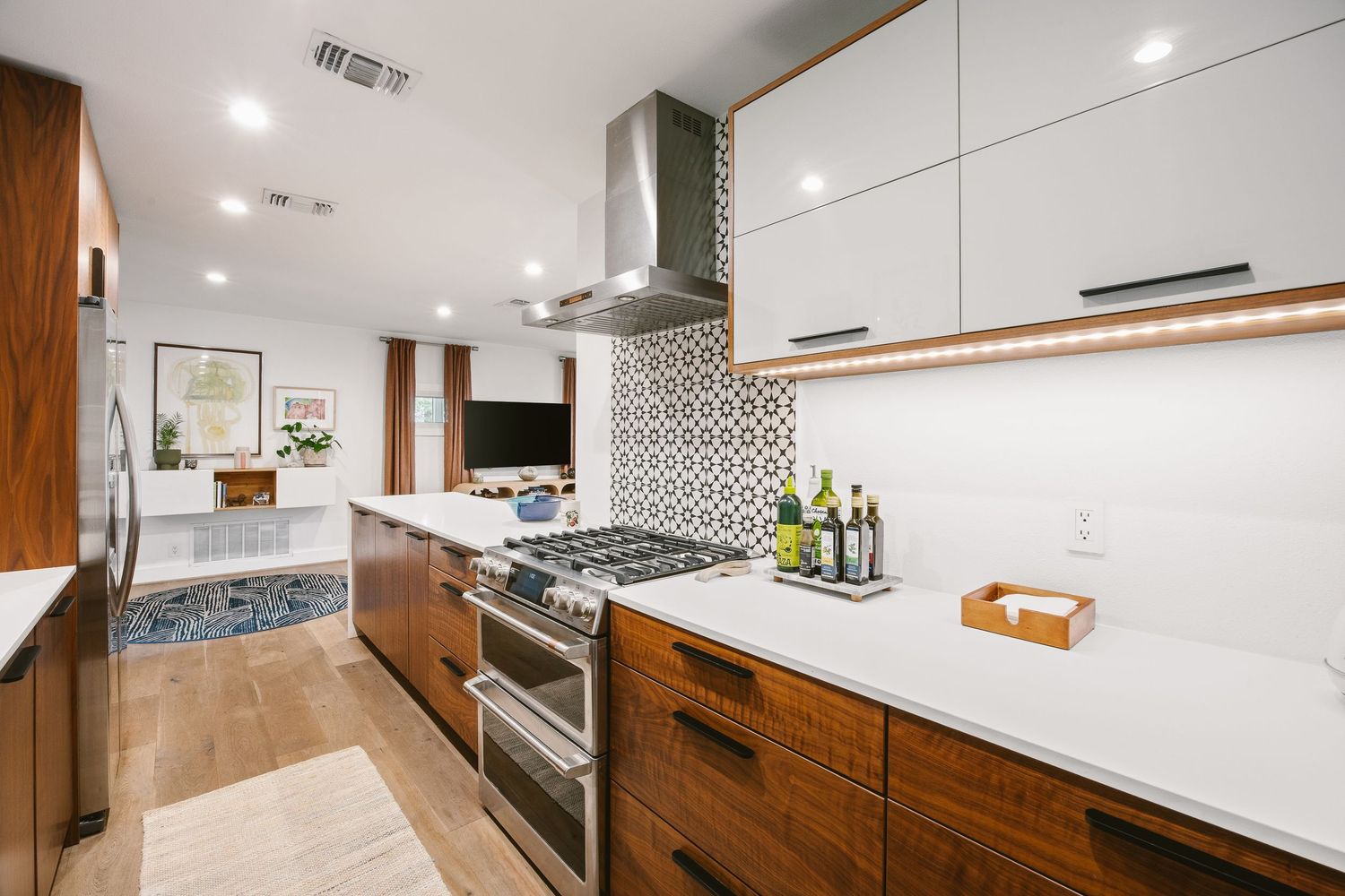 Modern kitchen with walnut cabinets, white uppers, stainless range, patterned tile backsplash, and quartz countertops.