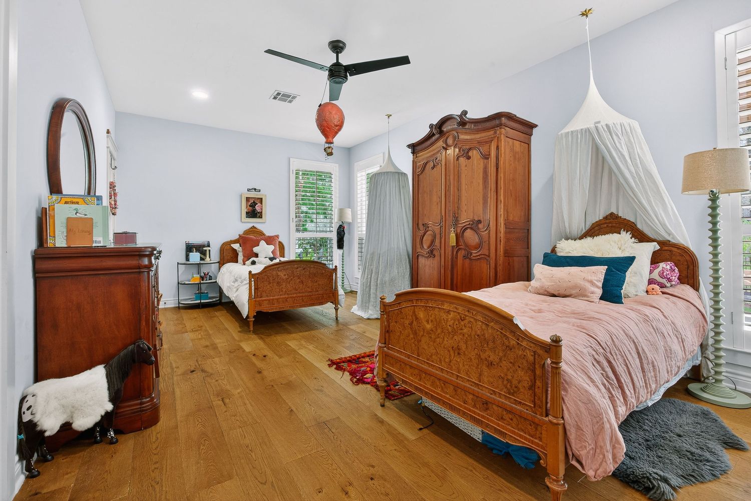 Elegant bedroom with antique wooden furniture, twin beds, hardwood floors, and a canopy draped over one bed.