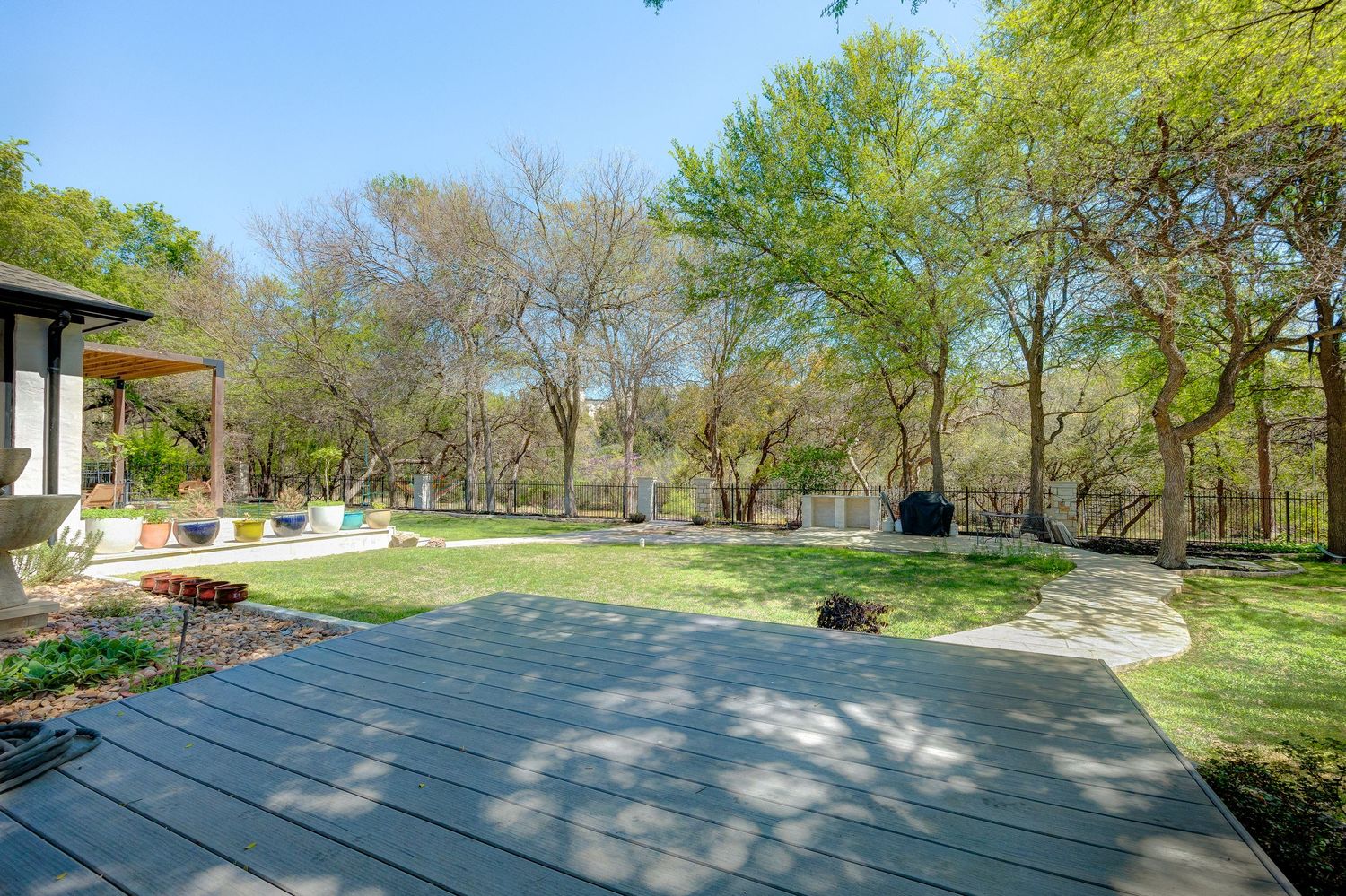 Spacious backyard deck with lush green trees, manicured lawn, and outdoor seating area on a sunny day.