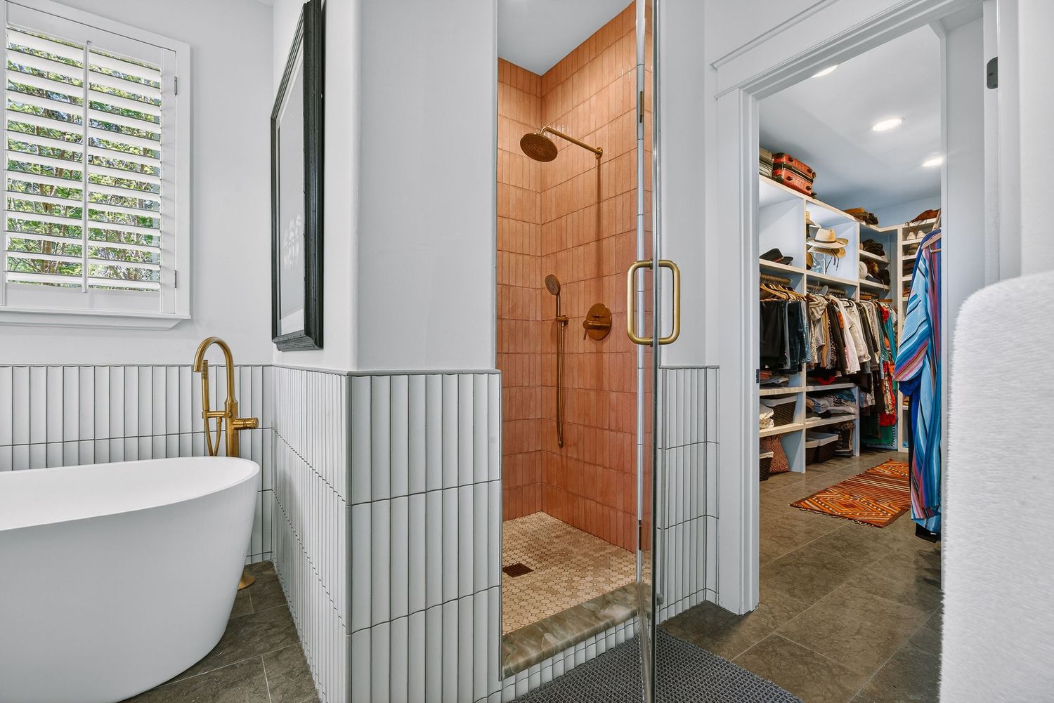 Modern bathroom with freestanding tub, terracotta tile shower, gold fixtures, and walk-in closet access.