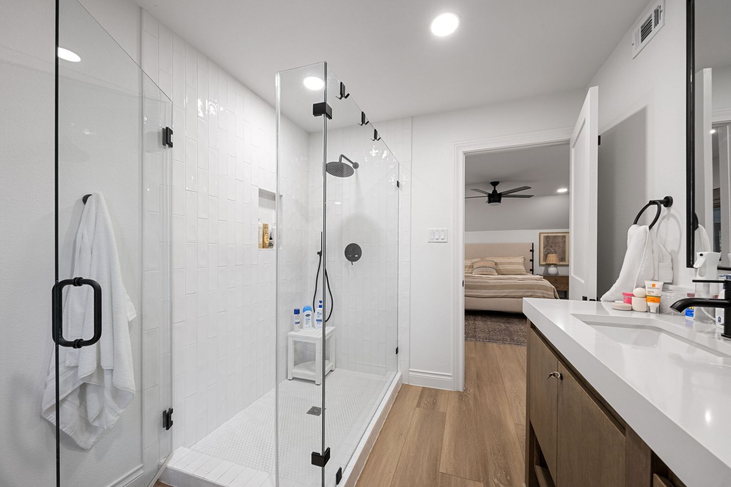 Modern bathroom featuring a glass-enclosed walk-in shower, wood-look flooring, and sleek black fixtures.