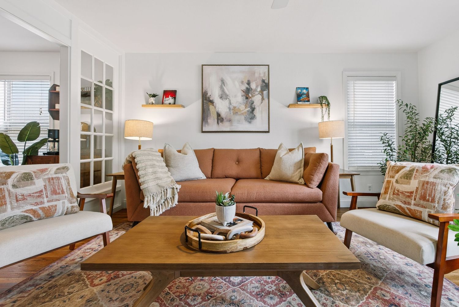 A bright and airy living room features a brown leather sofa, white walls, and natural decor elements.