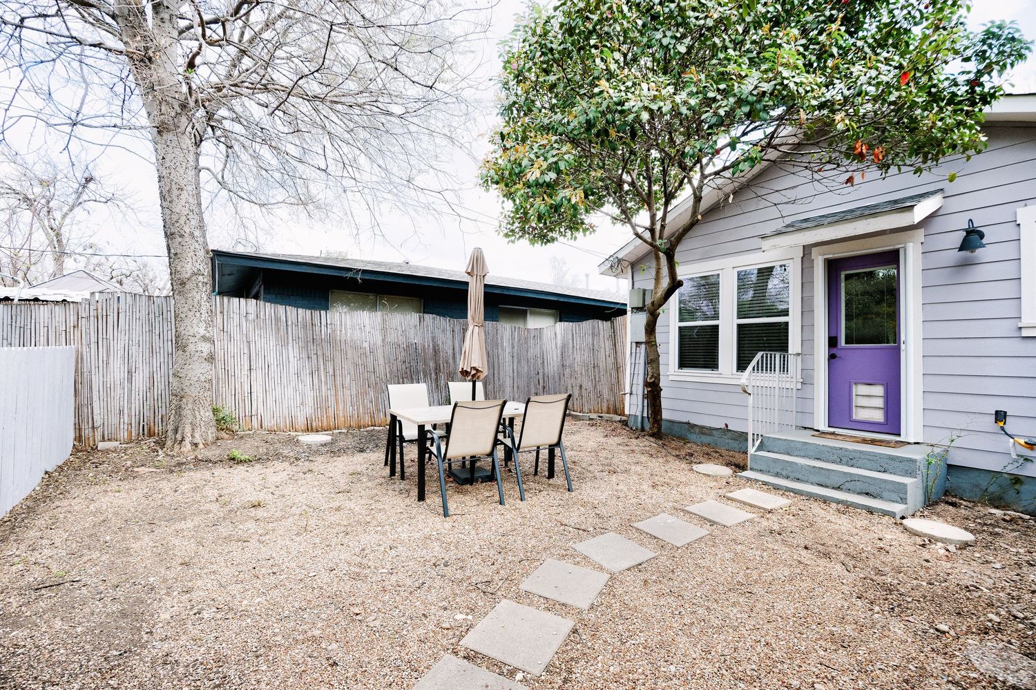 Panoramic view of a backyard with bare trees, wooden fencing, and stone pavers leading to a gray house exterior.