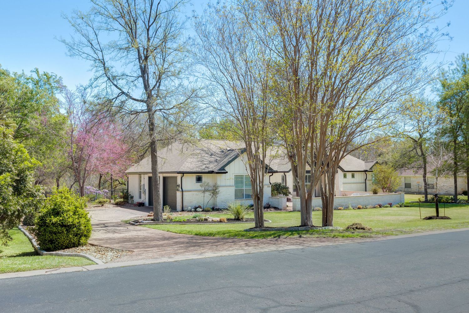 A suburban home surrounded by tall trees with a paved driveway and well-maintained lawn on a clear spring day.