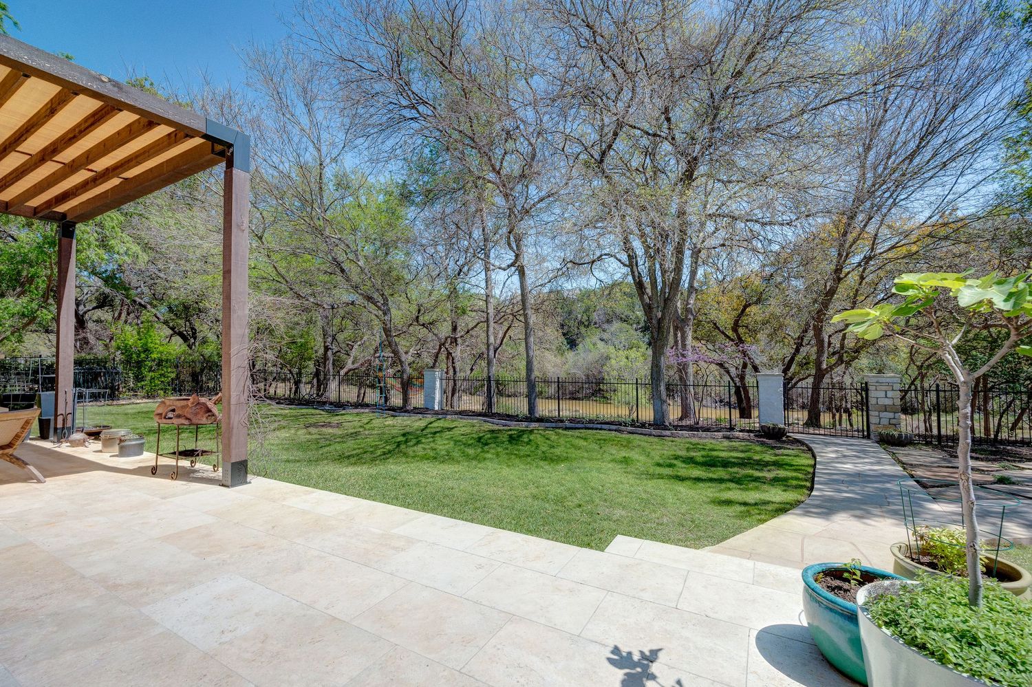 Spacious patio with pergola overlooking lush green backyard surrounded by mature trees and walking path.