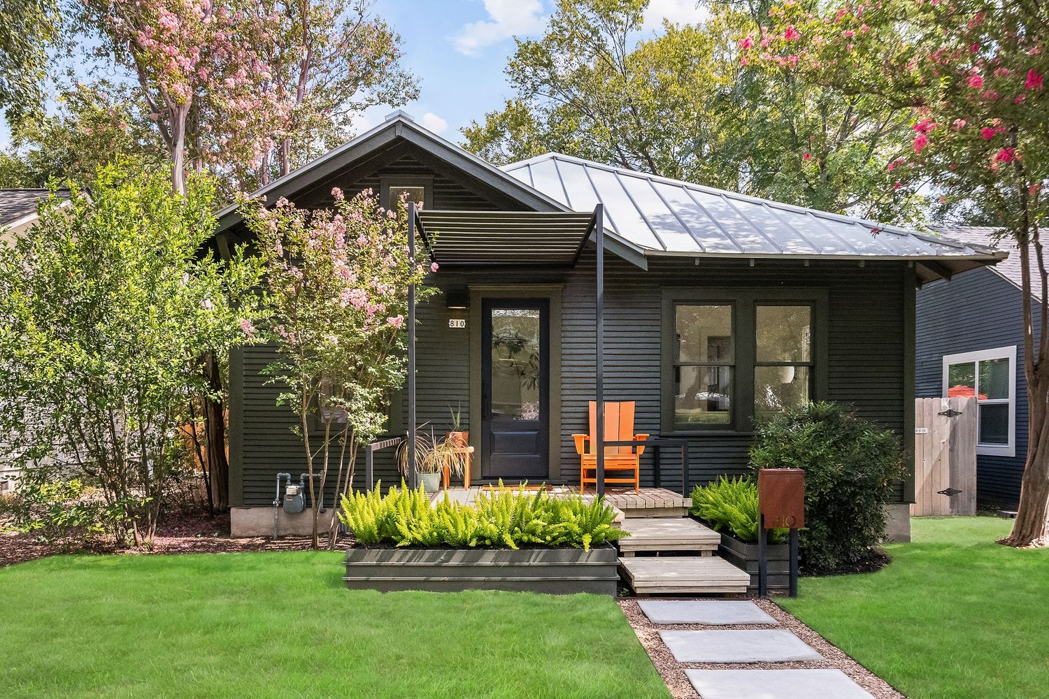 Charming dark gray cottage with metal roof, lush garden, and stone pathway.