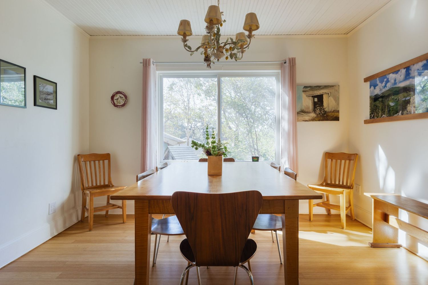 Dining area with chandelier, wooden chairs, and bright natural lighting from windows.