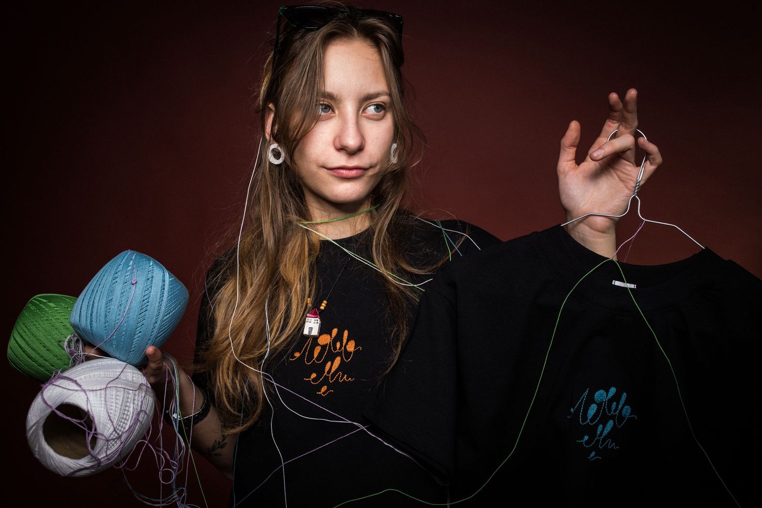 Young woman with gauge earrings holds colorful yarn balls while tangled in string, wearing black sweater.