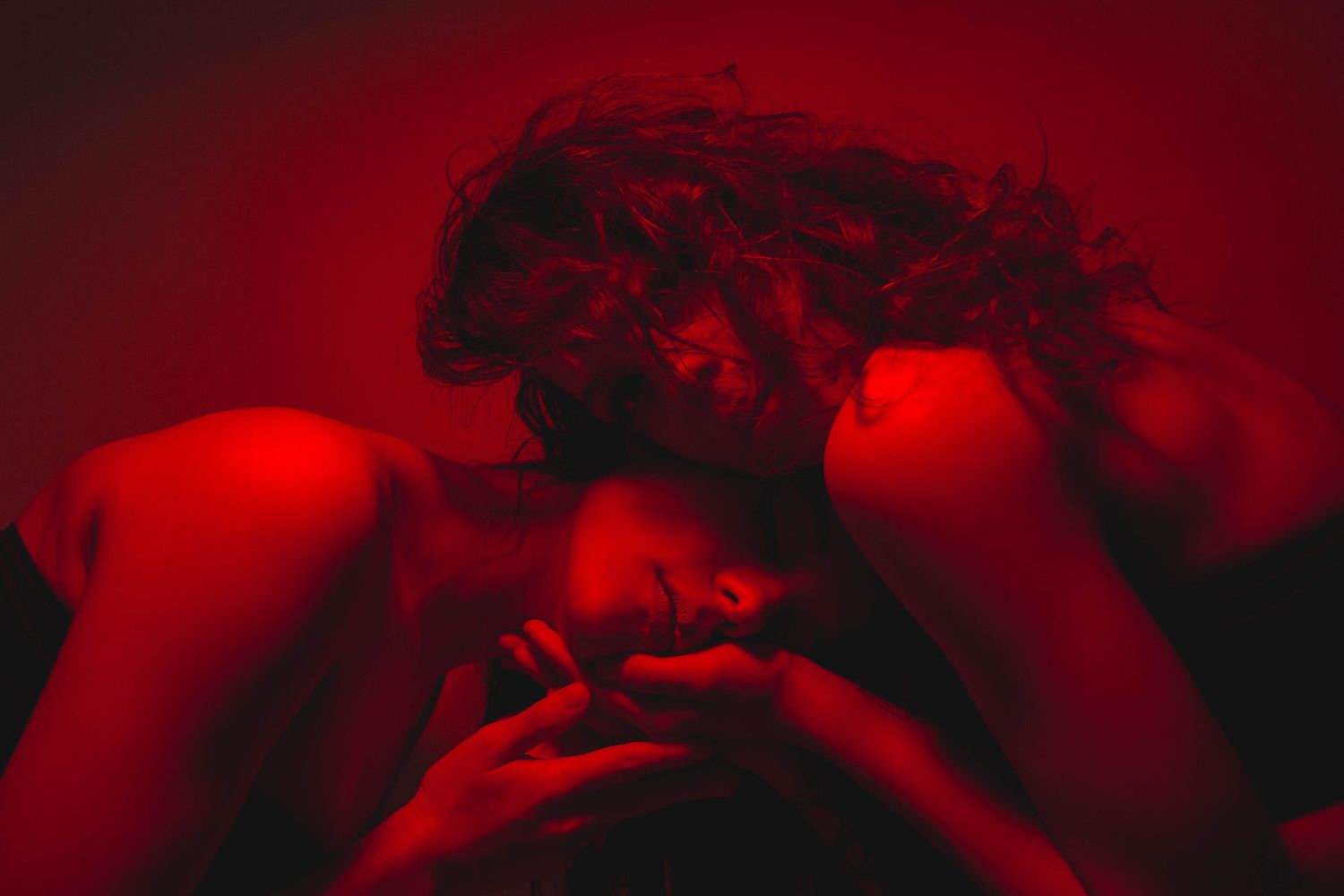 Person lying back with curly hair spread, hands clasped, dramatically lit in deep red light.