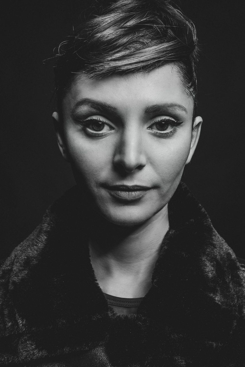 Black and white close-up portrait of short-haired woman in fur coat against dark background.