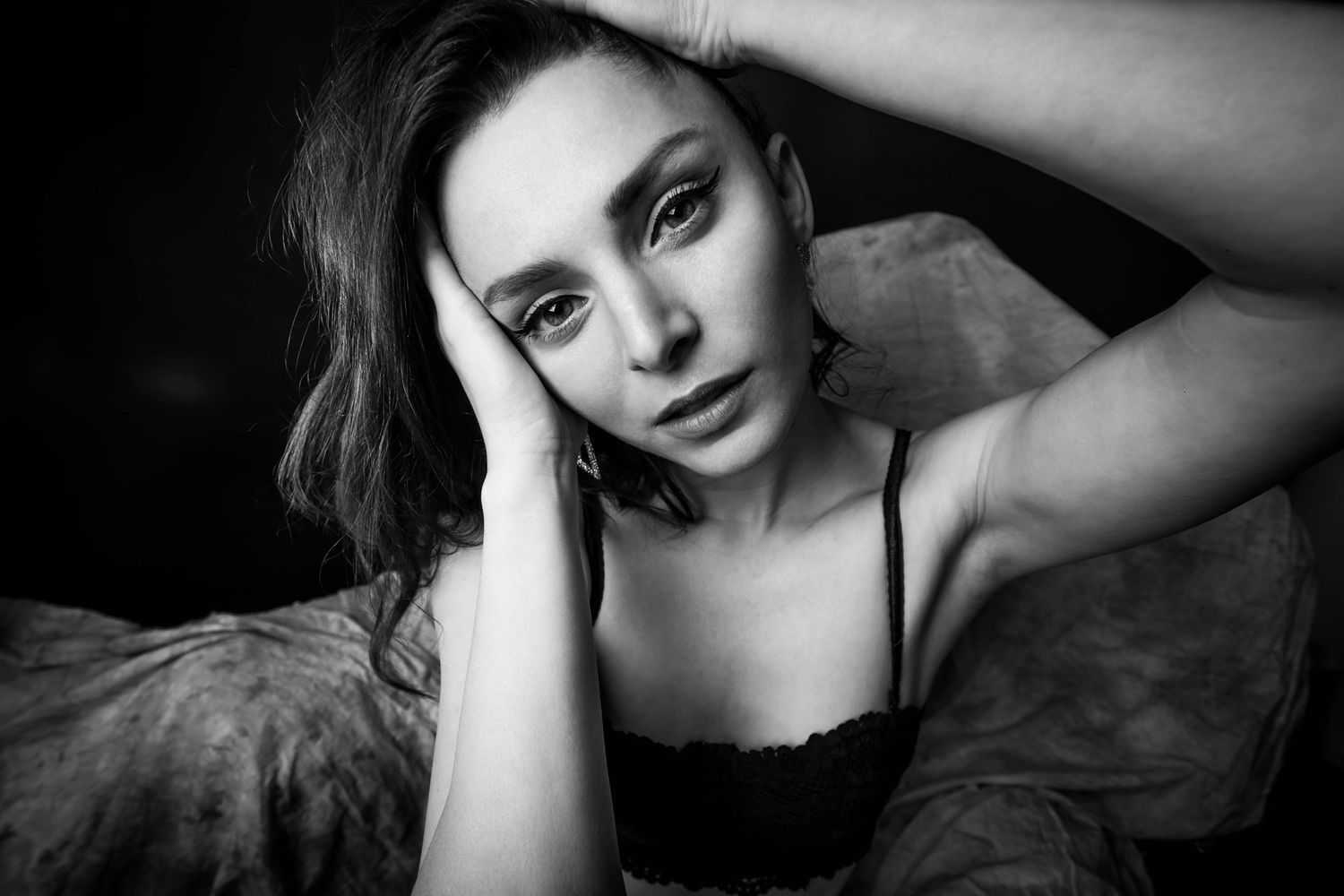Black and white portrait of young woman resting head on hands, gazing at camera with soft expression.