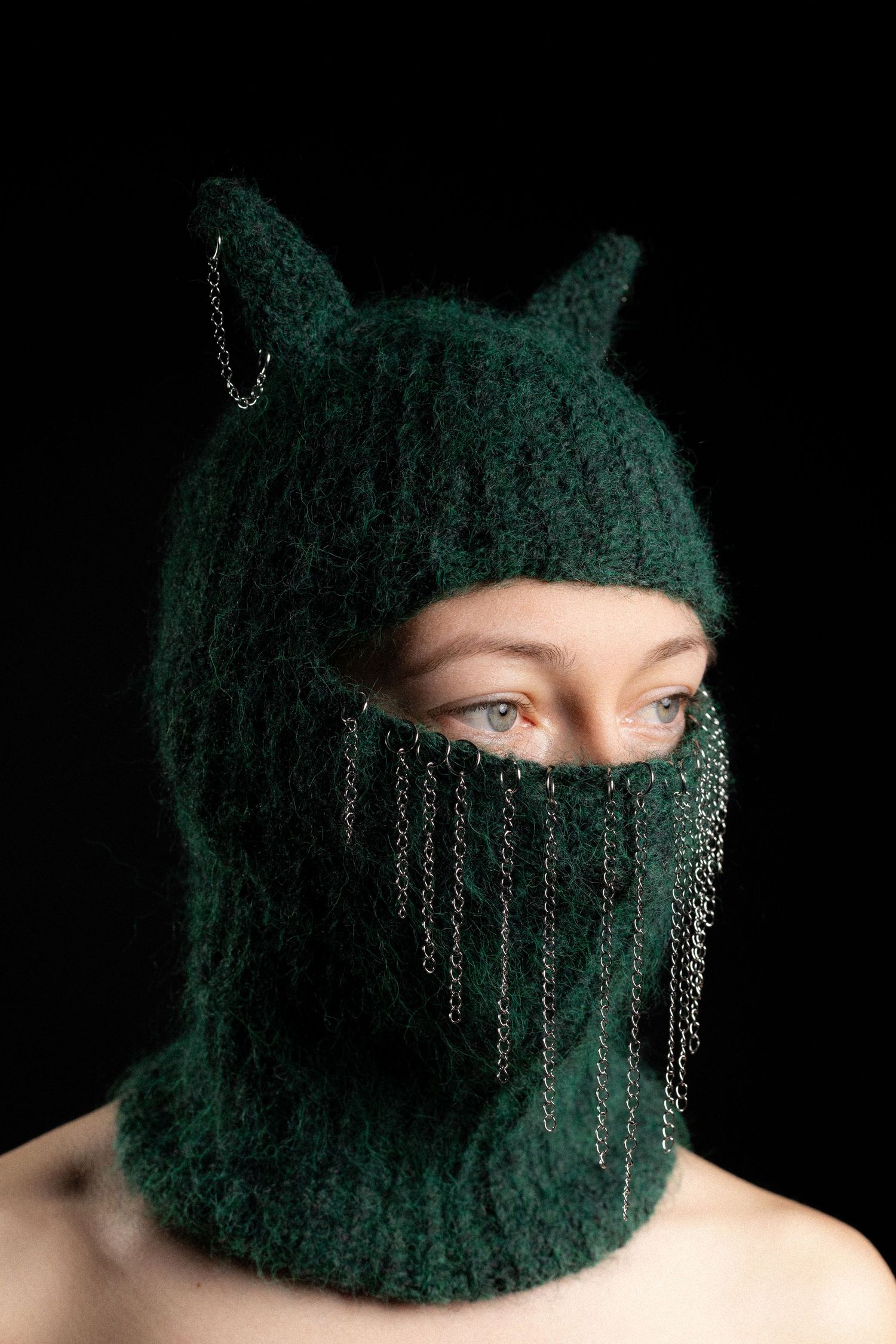 Woman wearing dark green fuzzy balaclava with cat ears and silver chain fringe details.
