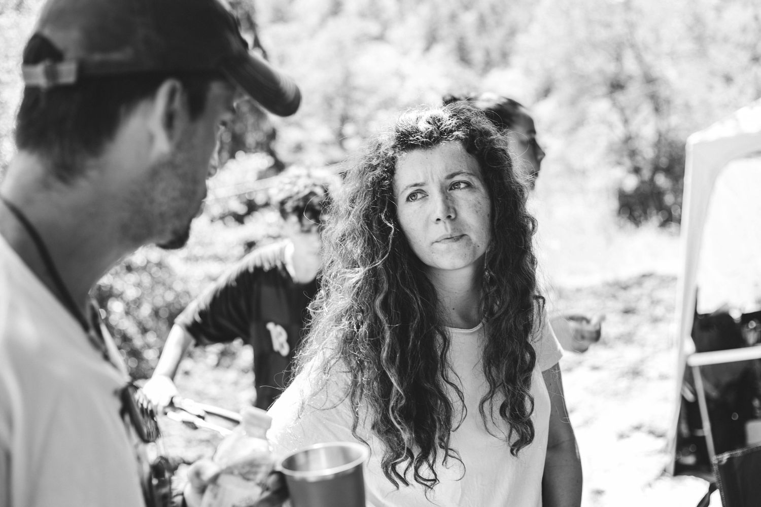 Curly-haired woman listens attentively on a black and white outdoor film production set.