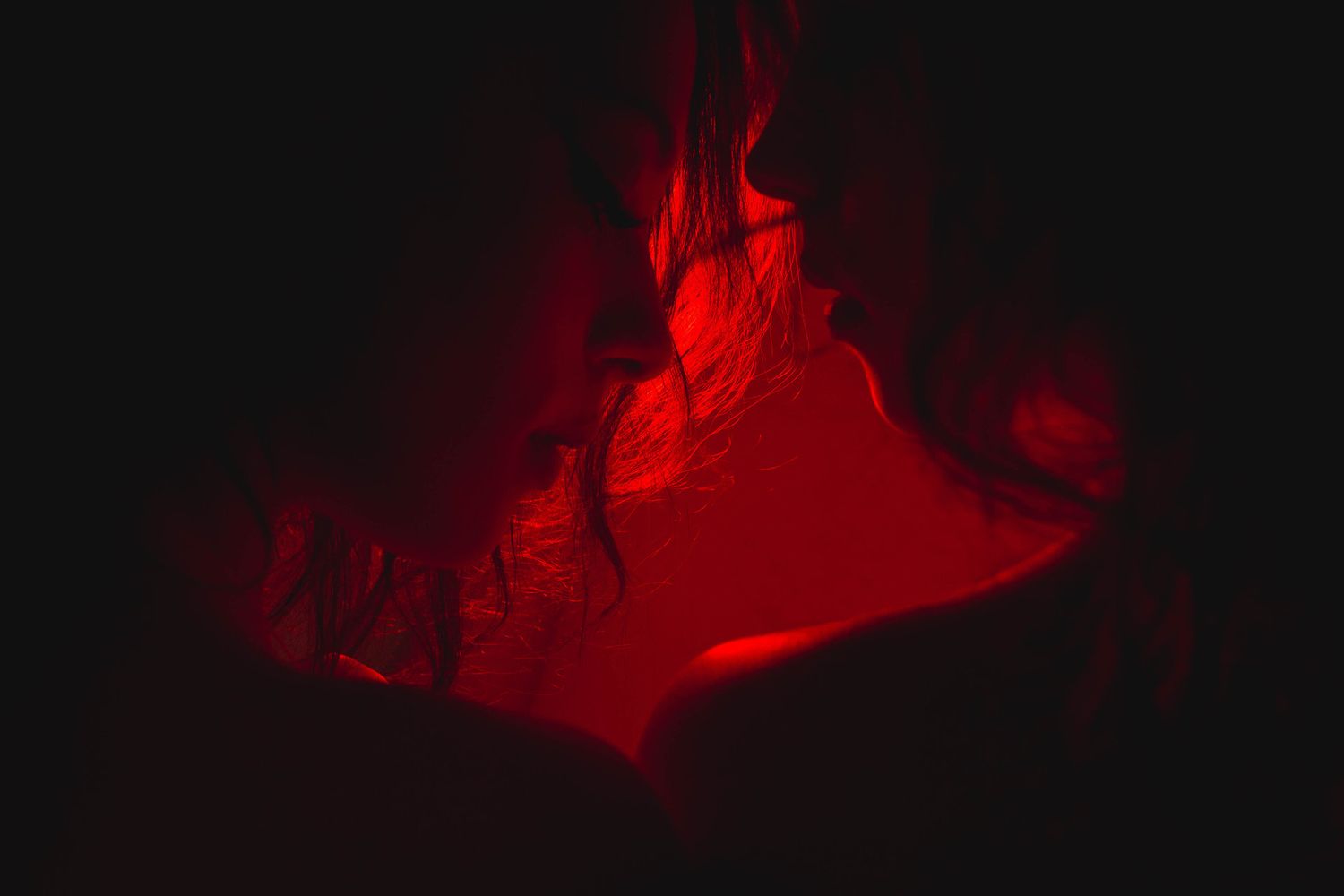 Abstract dark image illuminated by dramatic red light revealing flowing fabric textures.