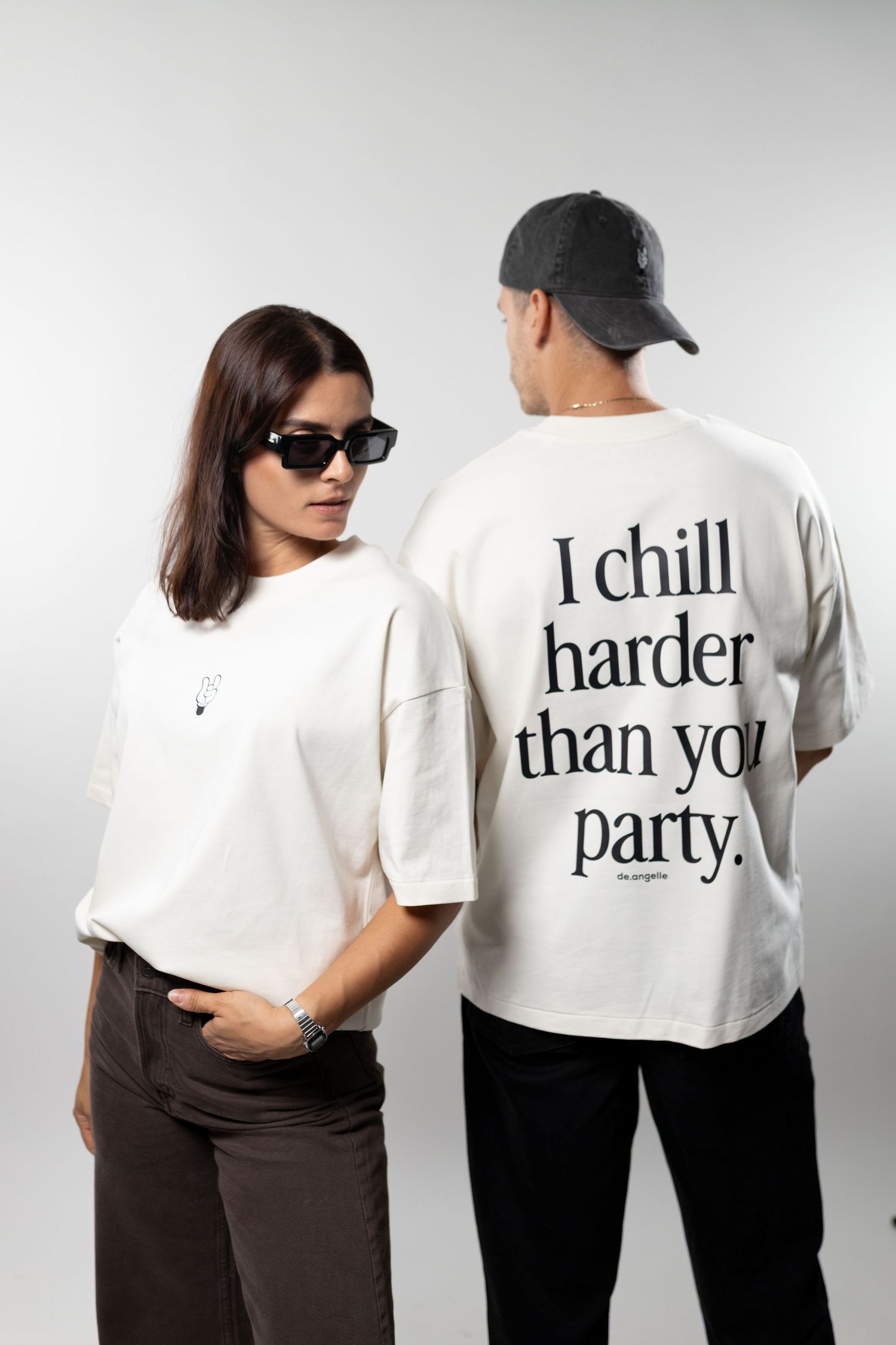 Two models wearing oversized white graphic tees, one reading 'I chill harder than you party' on the back.