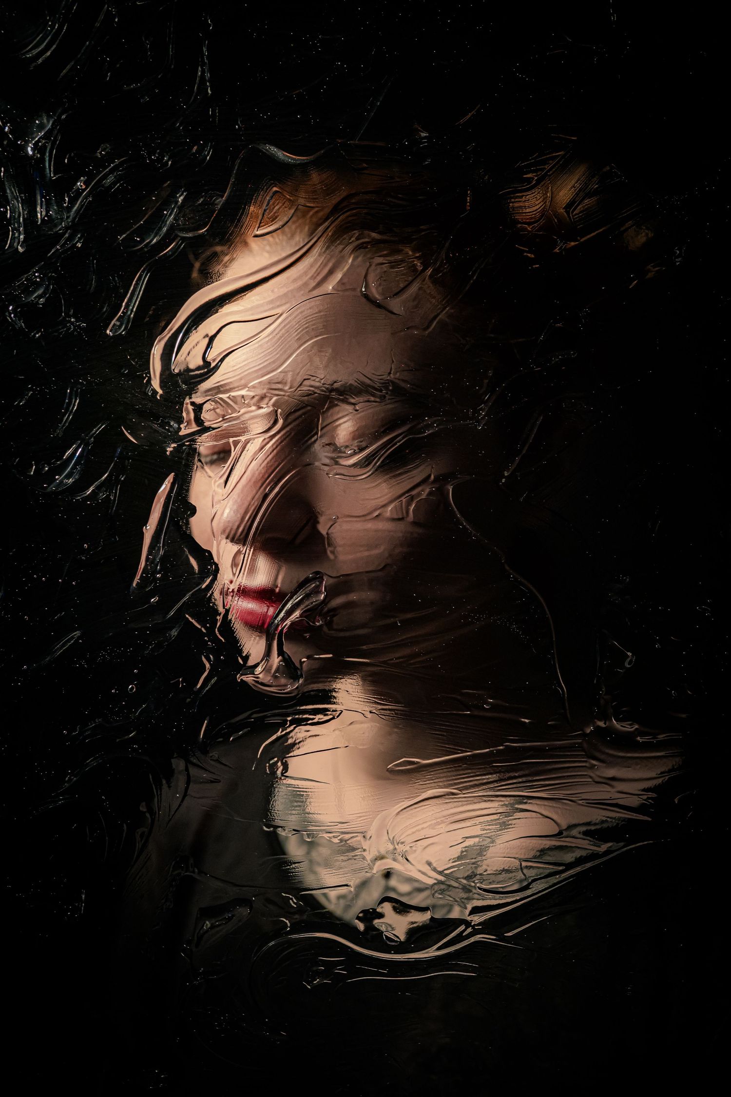 Ethereal dark portrait of woman with closed eyes pressed against wet glass creating surreal distortion.