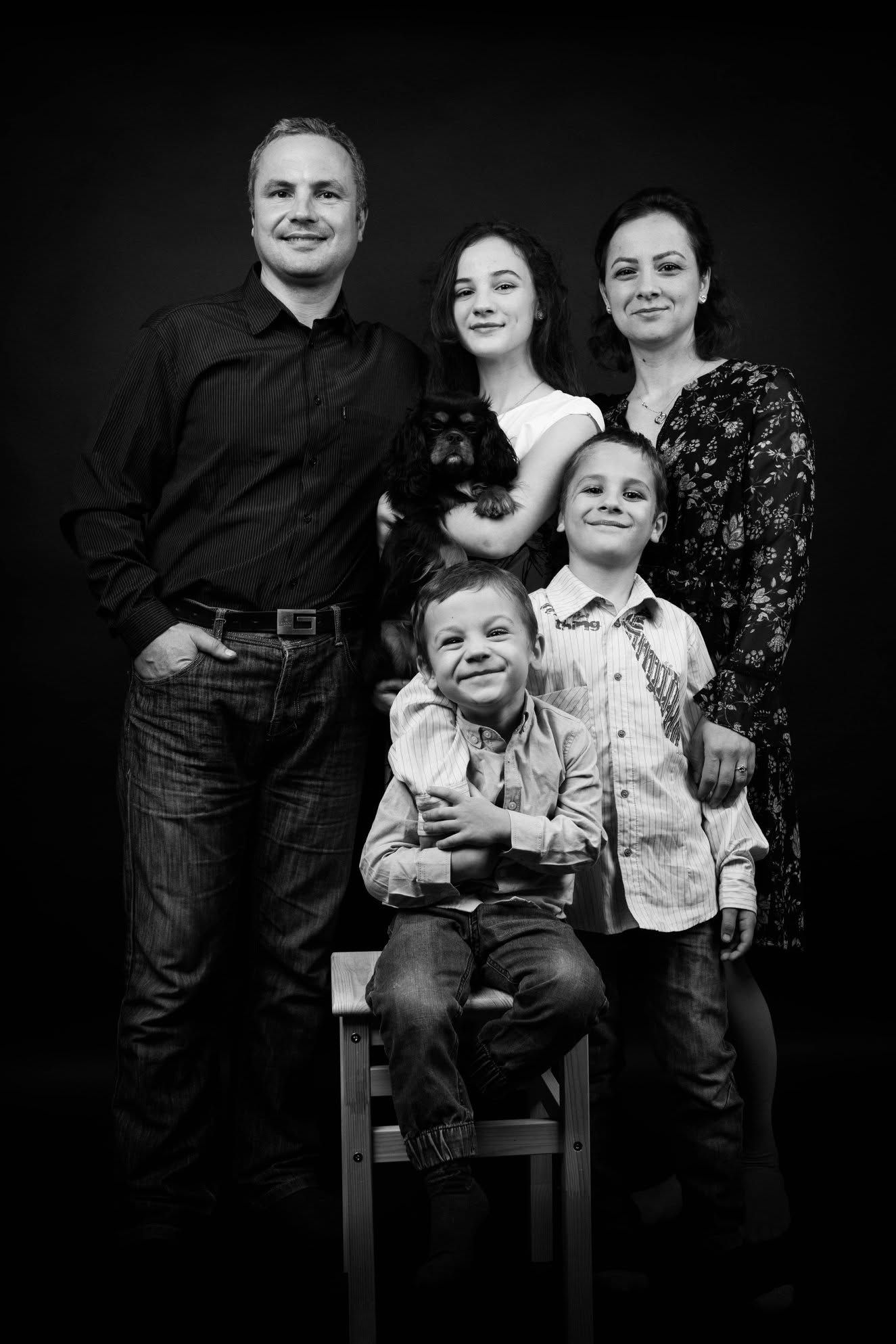 Black and white family portrait of parents with three children, one seated on a stool, posed against dark studio background.