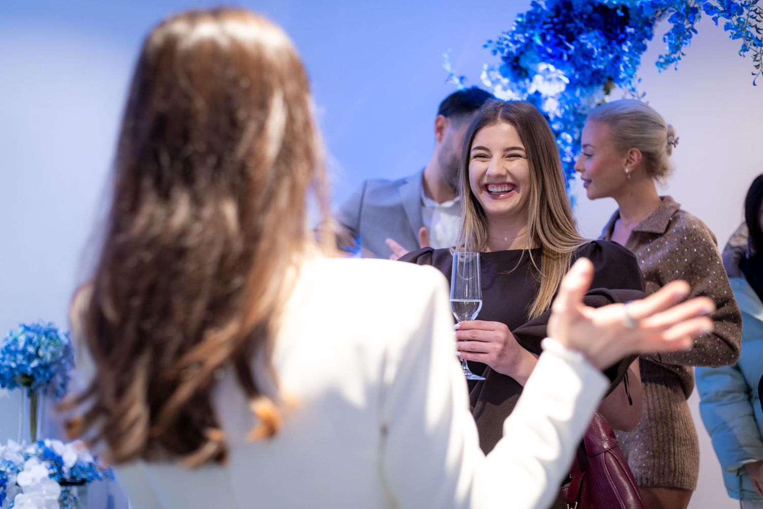 Guests socializing and laughing with champagne glasses at elegant blue-themed cosmetics launch party.