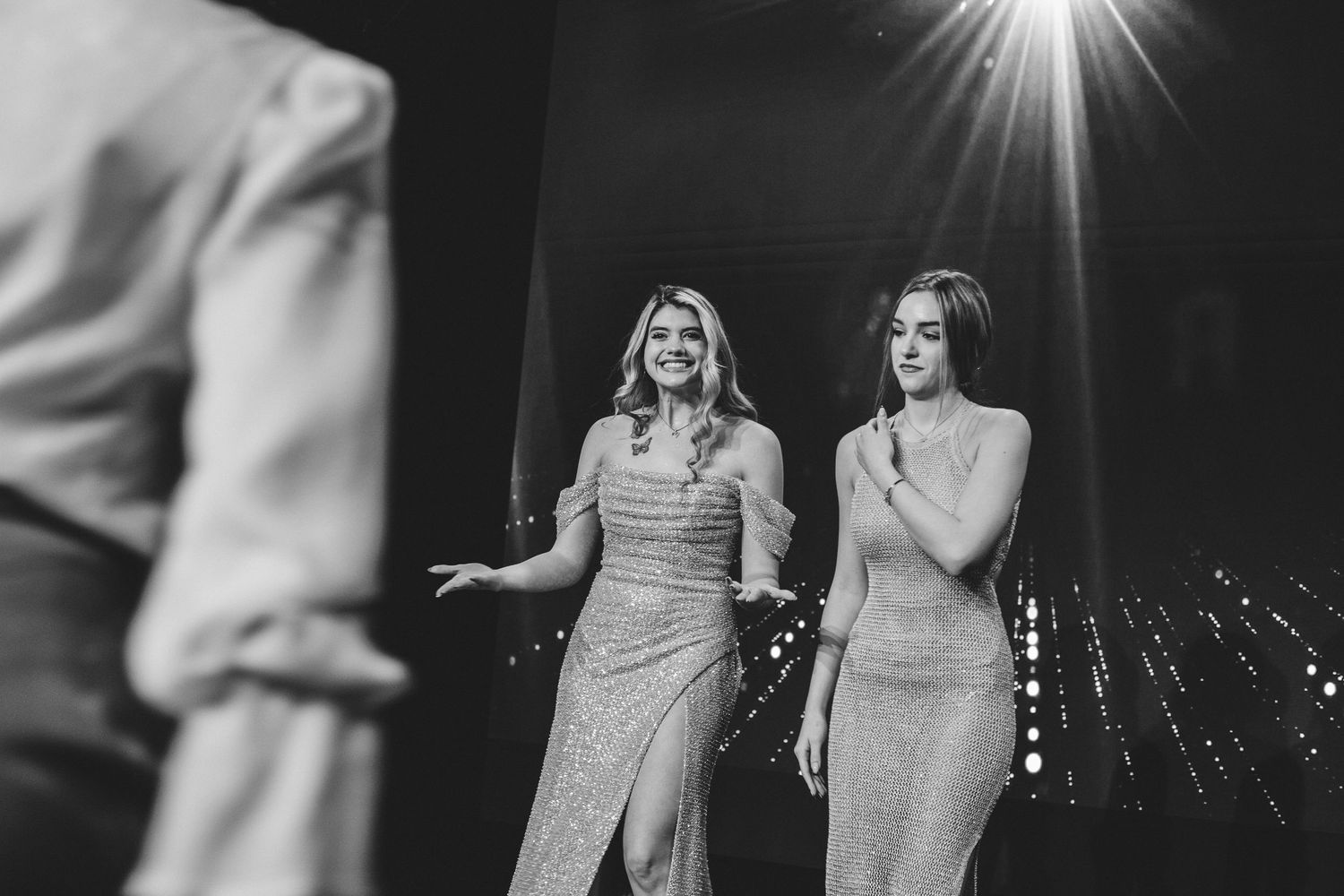 Two elegant women in sparkly gowns on stage in black and white photo.