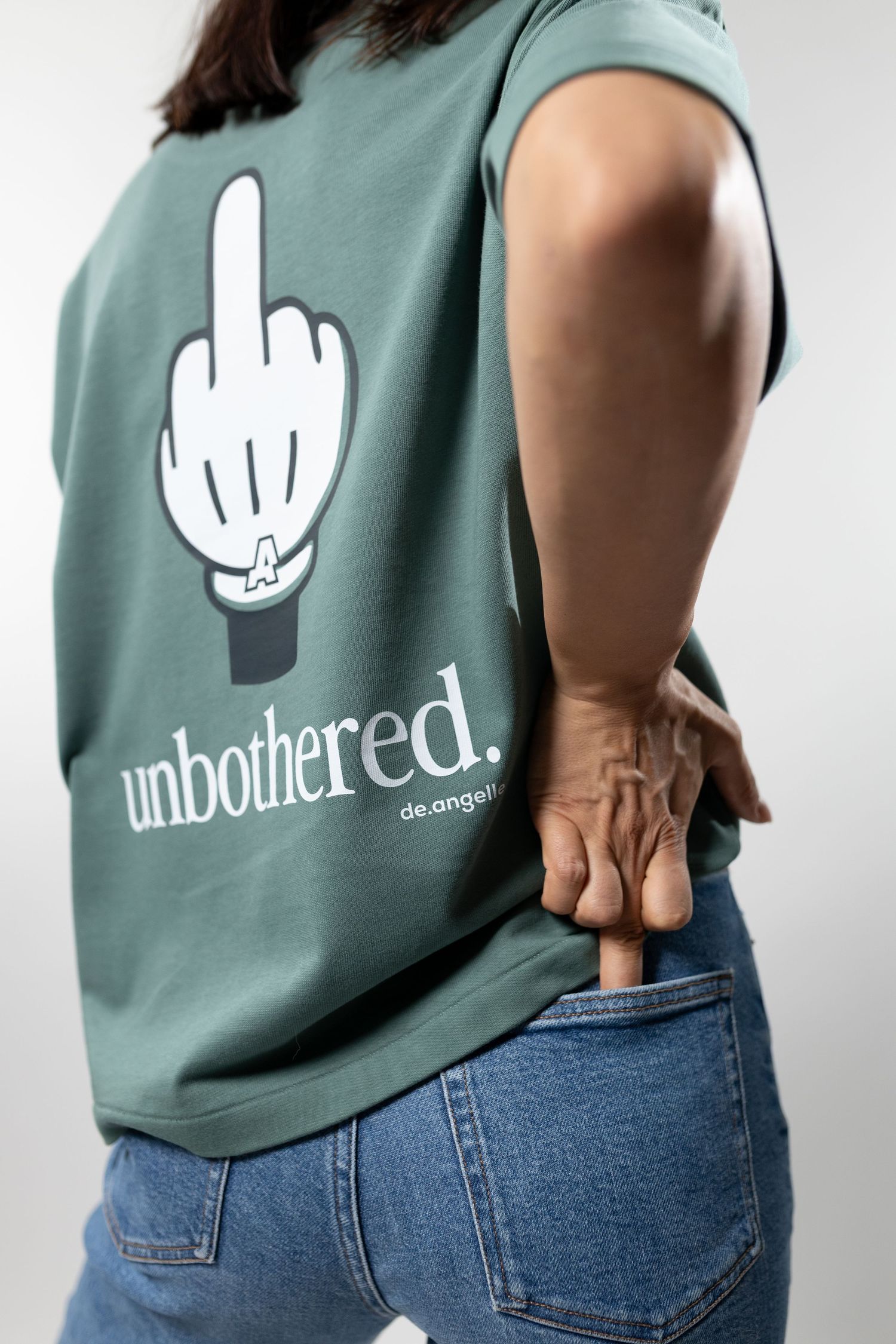 Woman wearing green 'Unbothered' graphic tee with middle finger print, paired with blue jeans, back view.