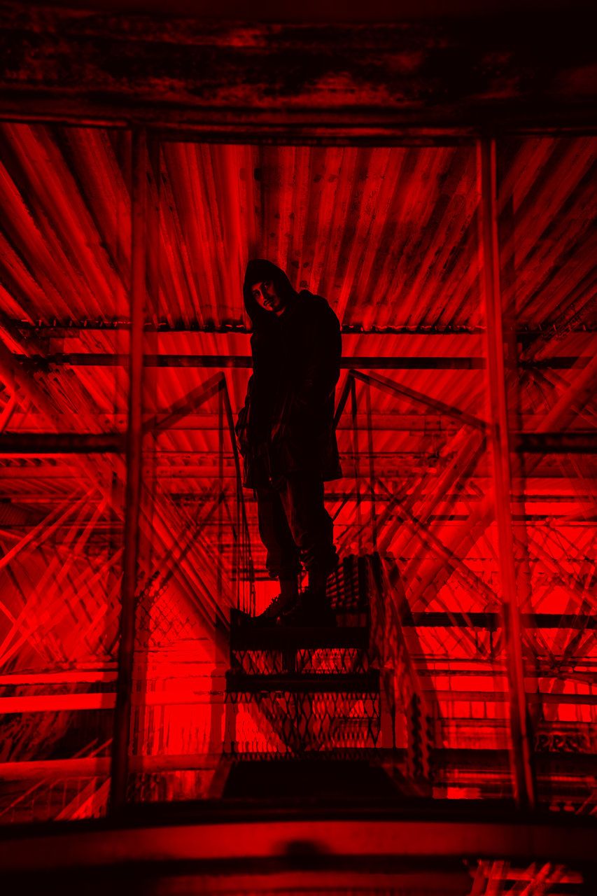 Silhouetted person standing on scaffolding dramatically lit in vivid red light against dark background.