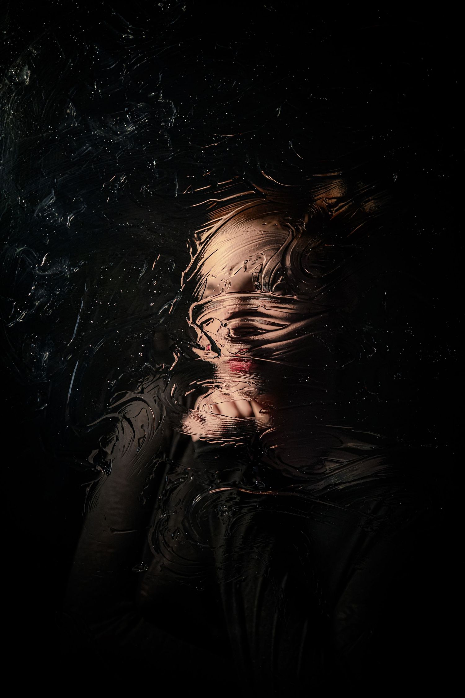 Surreal dark portrait of person pressed against wet glass, distorting facial features dramatically.