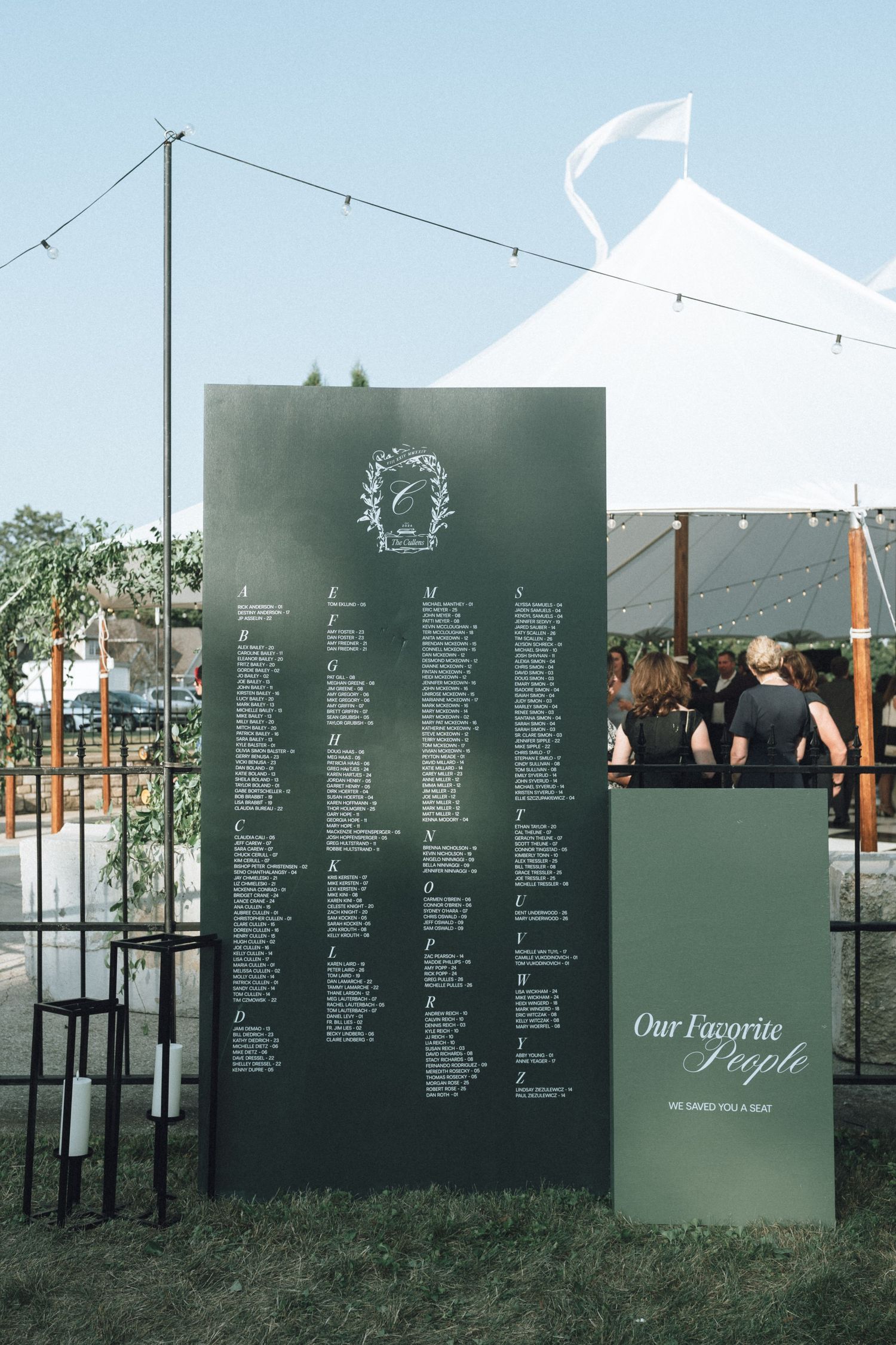 Modern wedding seating chart displayed on dark green panels with white text in an outdoor garden setting.
