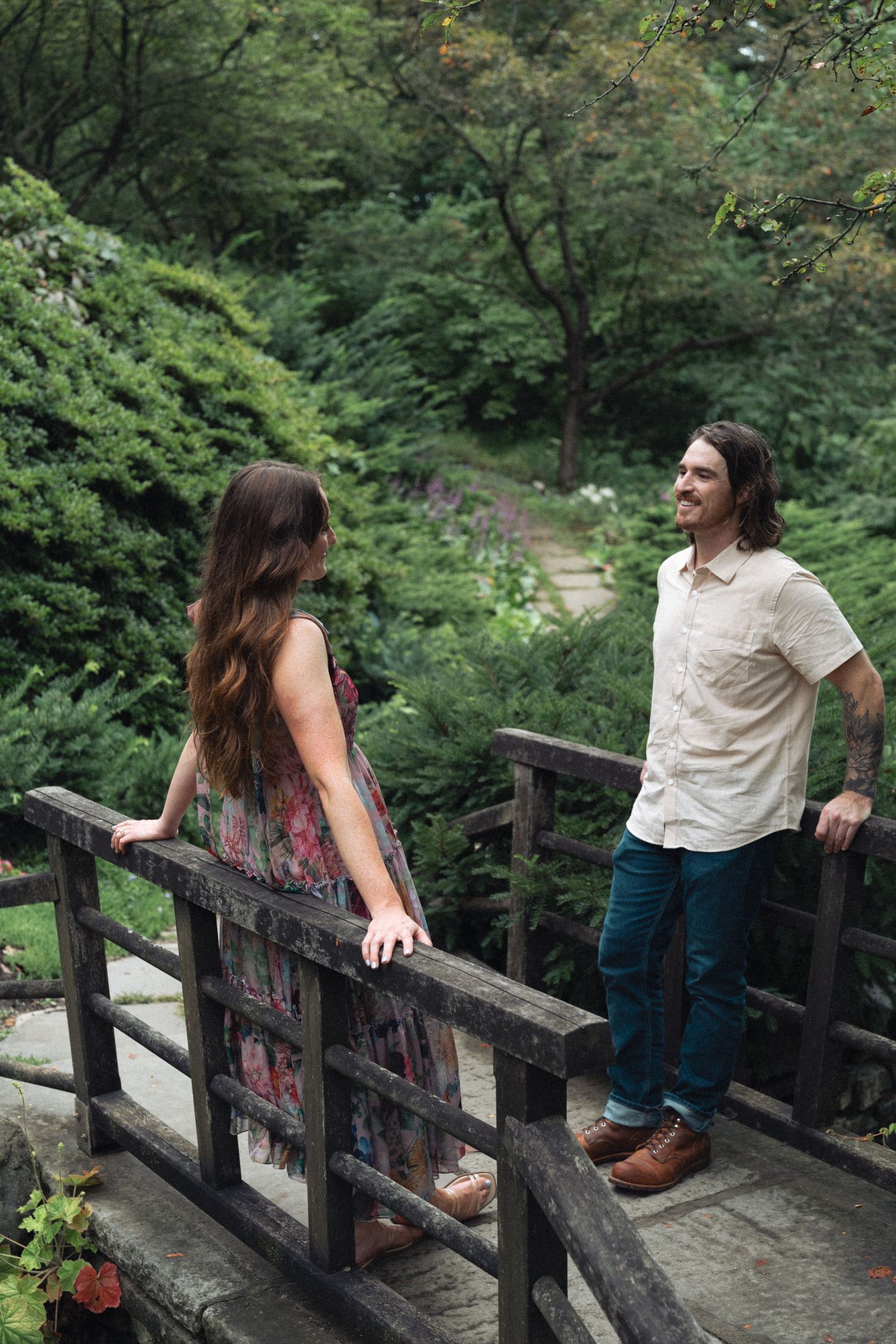 Couple flirting across a wooden bridge railing in a lush green forest setting in Indianapolis