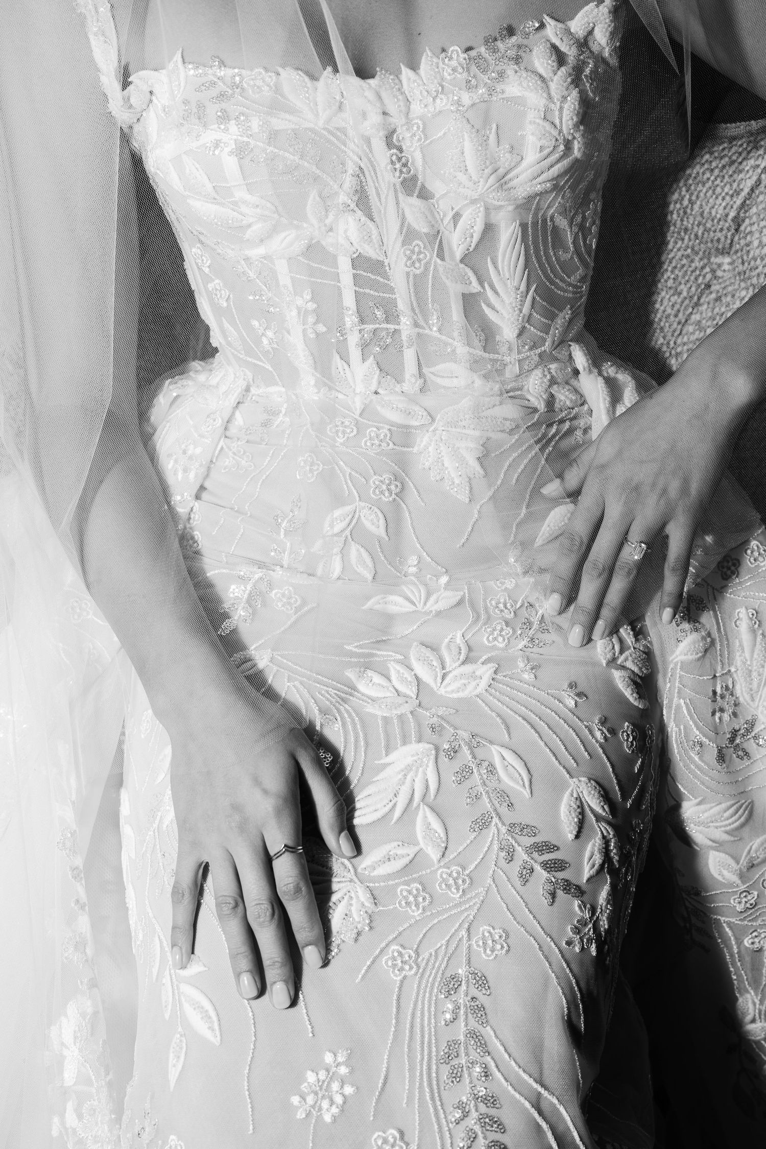 Close-up details of delicate white lace and floral embroidery on wedding dress fabric with hands gently touching the material.