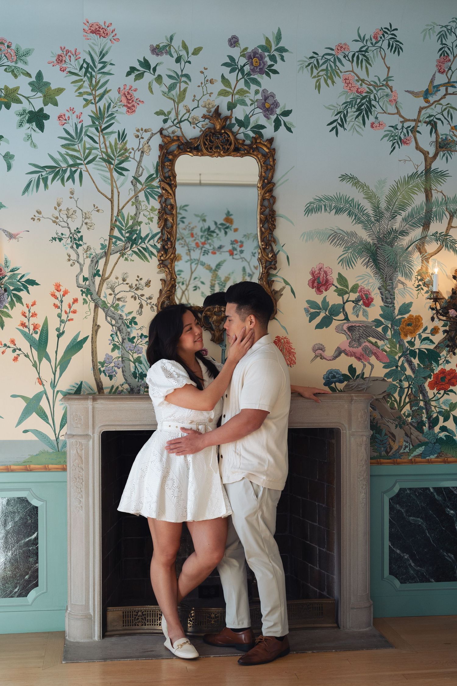 A romantic series of poses captured in a room with floral wallpaper and white fireplace showing a couple dancing and embracing.