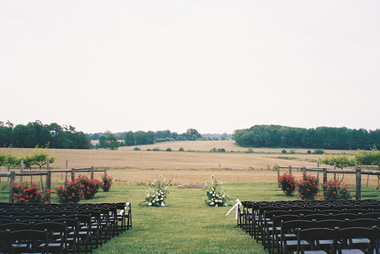 Outdoor wedding ceremony setup with dark chairs, floral arrangements, and a scenic Kentucky winery landscape