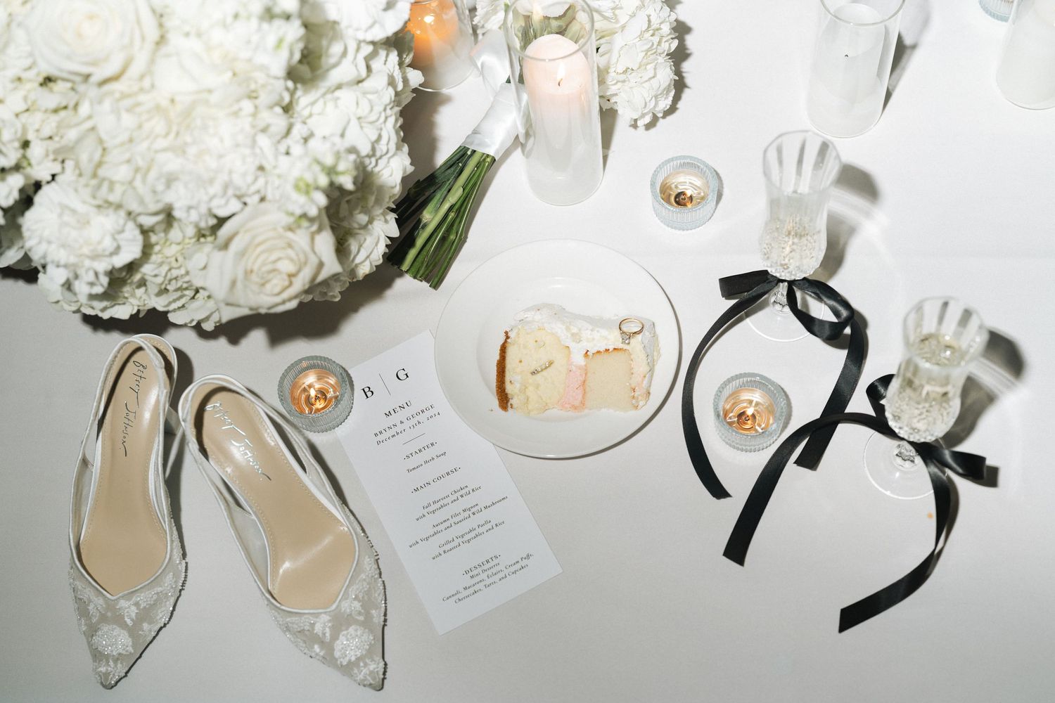 Elegant wedding reception table settings with white decor, menus, flowers and candles arranged beautifully on white tablecloths.