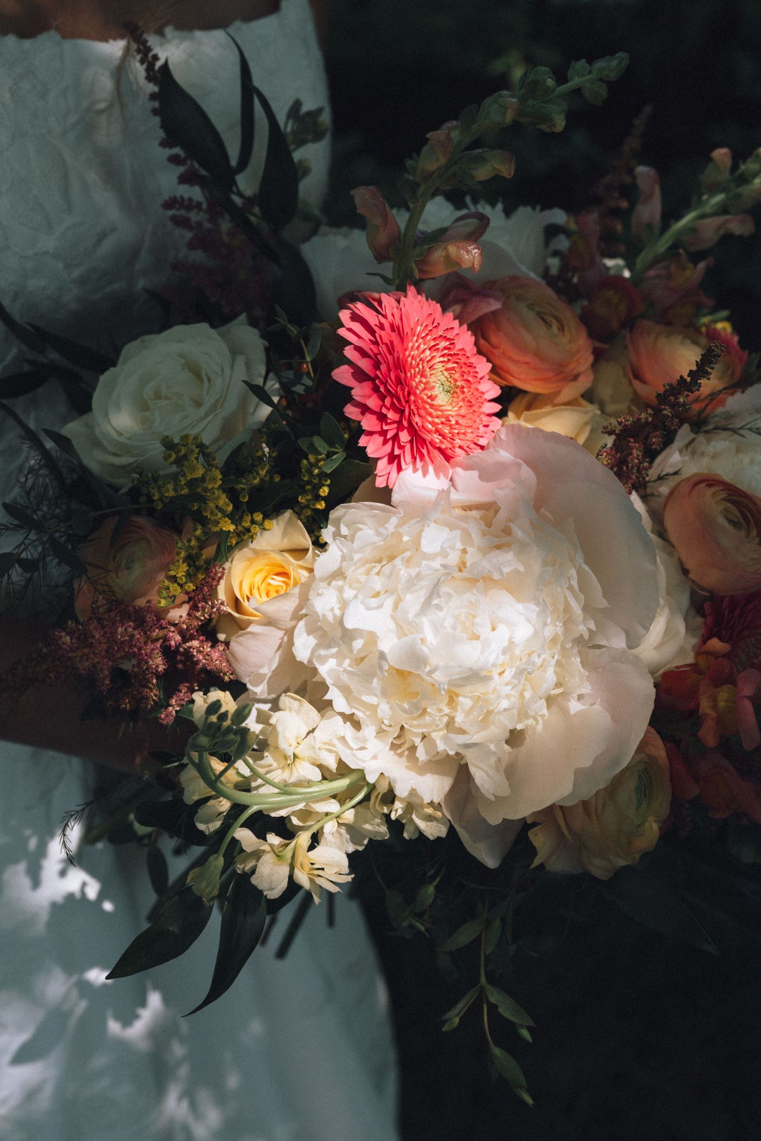 Bride holding a lush wedding bouquet featuring white peonies, coral gerbera daisy, peach roses, and greenery in Indianapolis