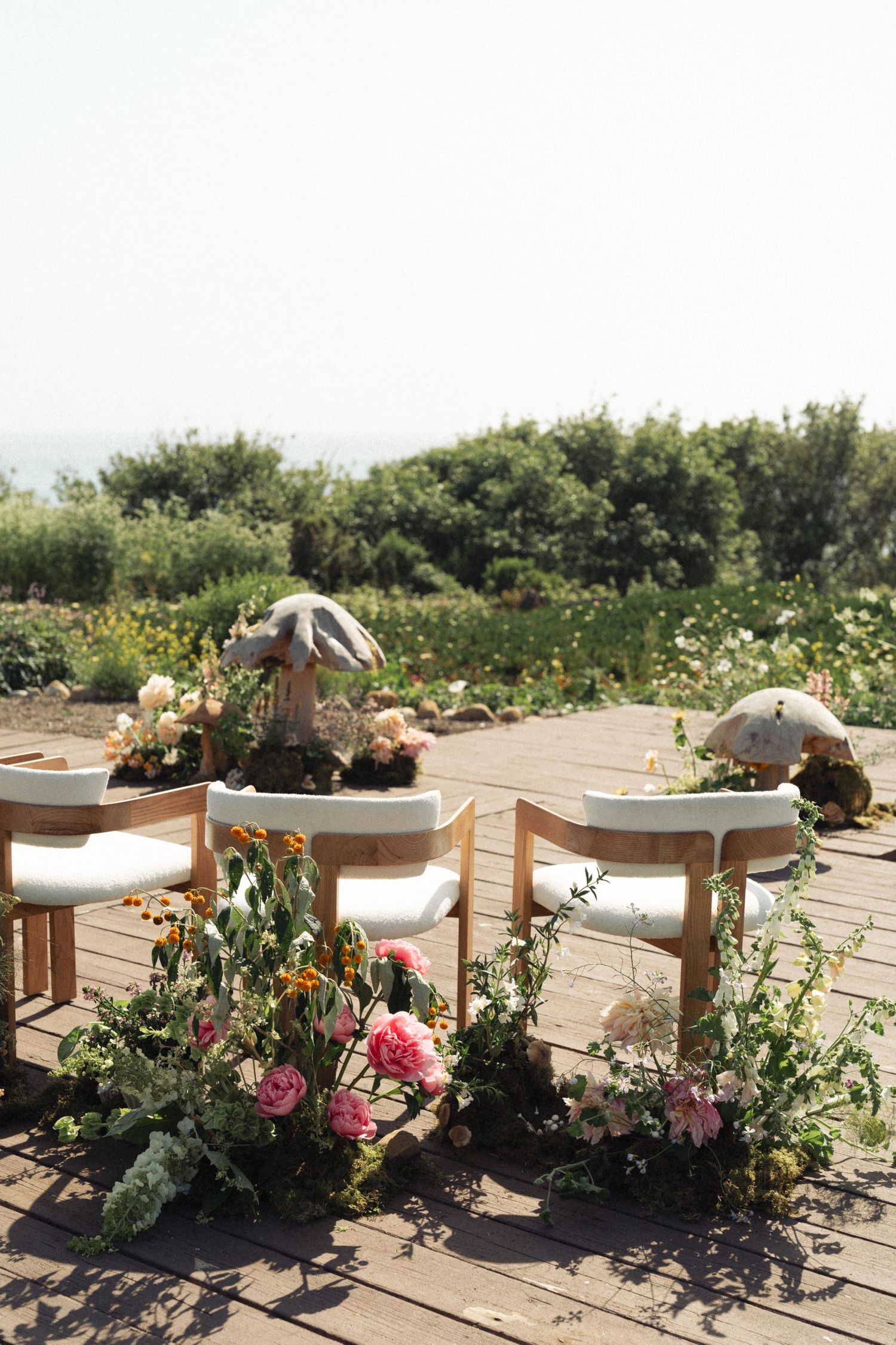 Wooden chairs decorated with pink and peach floral arrangements on an outdoor patio with garden views in California