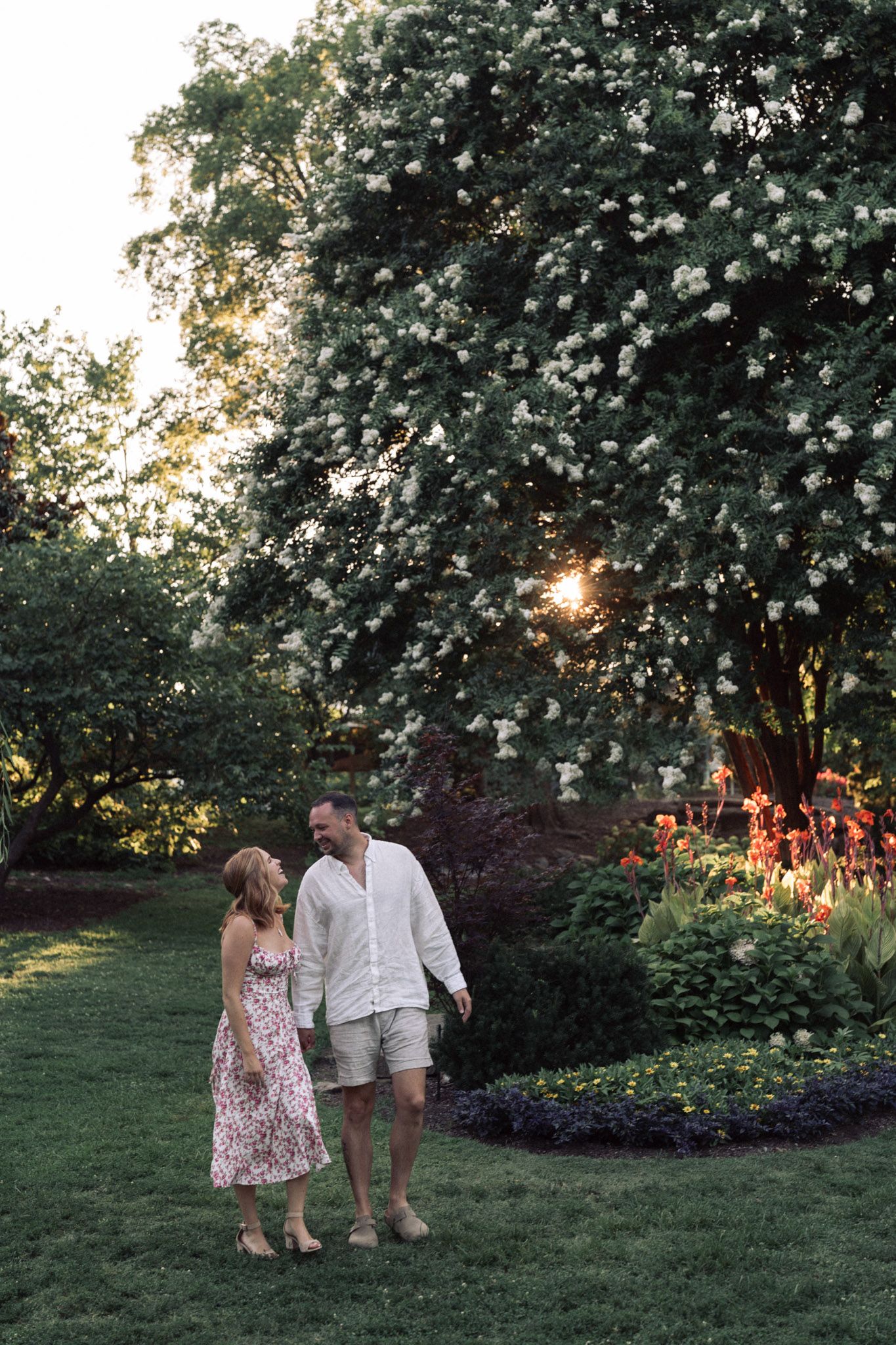 Two figures explore a lush garden backlit by golden evening sunlight filtering through leafy trees in Nashville