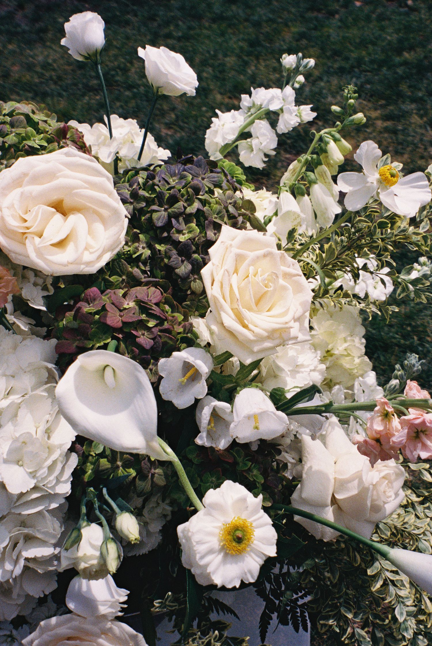 Elegant white floral arrangement featuring roses, calla lilies, hydrangeas, and poppies with lush greenery captured on vintage film