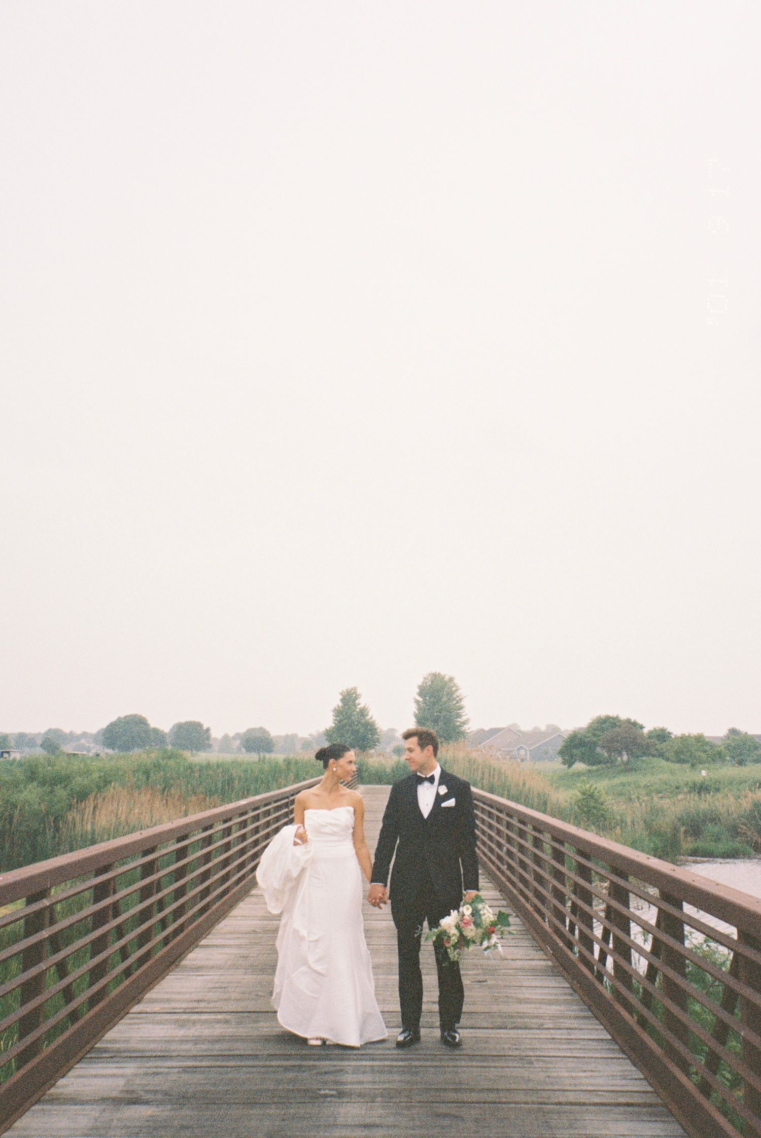 A couple in wedding attire walks along a rustic wooden bridge together in a romantic outdoor setting in Chicago