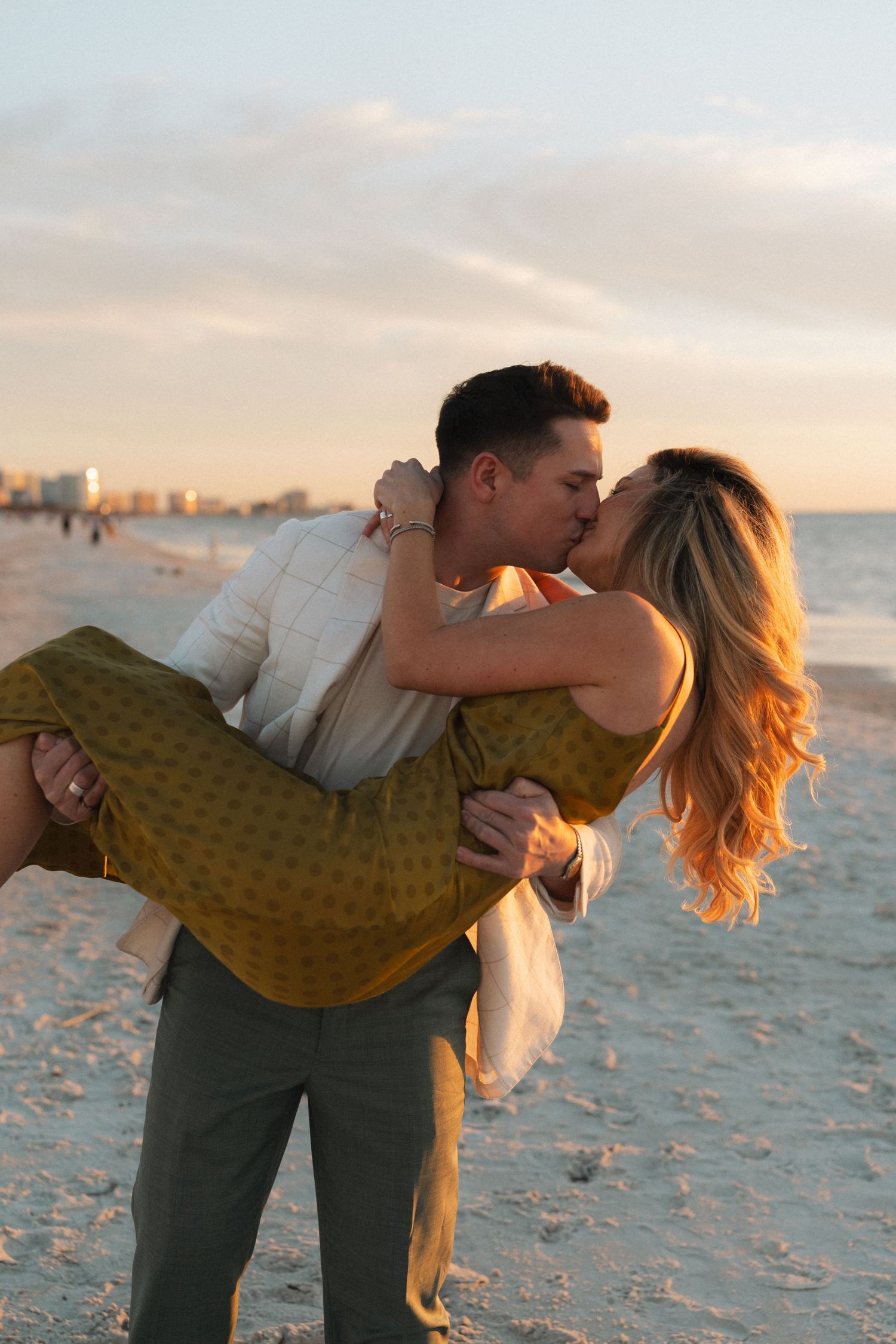 A romantic couple shares a tender moment at sunset on a sandy beach in Clearwater, Florida as golden light illuminates the scene.