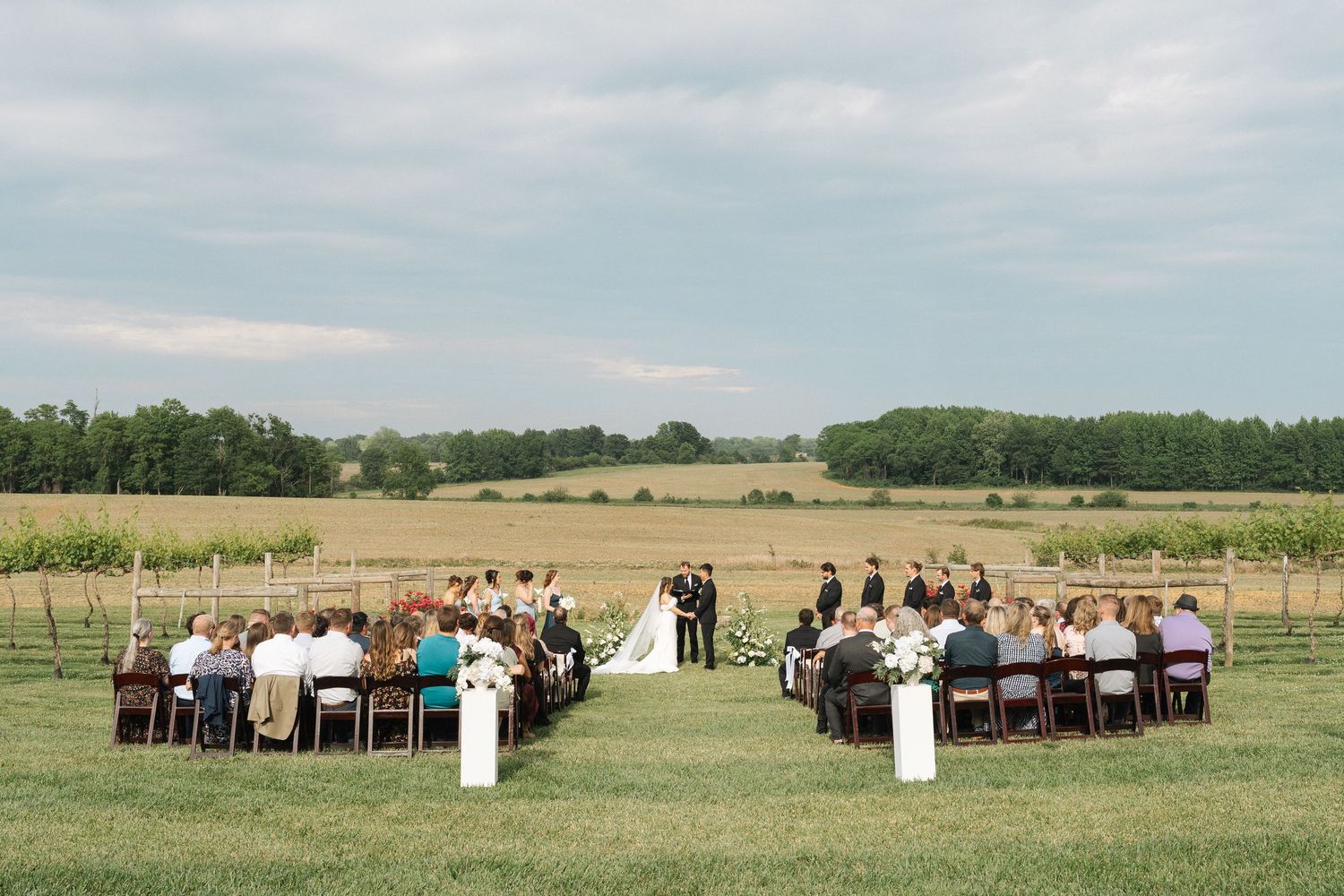 Outdoor wedding ceremony in a grassy field with guests seated in rows on both sides as a couple exchanges vows in Kentucky